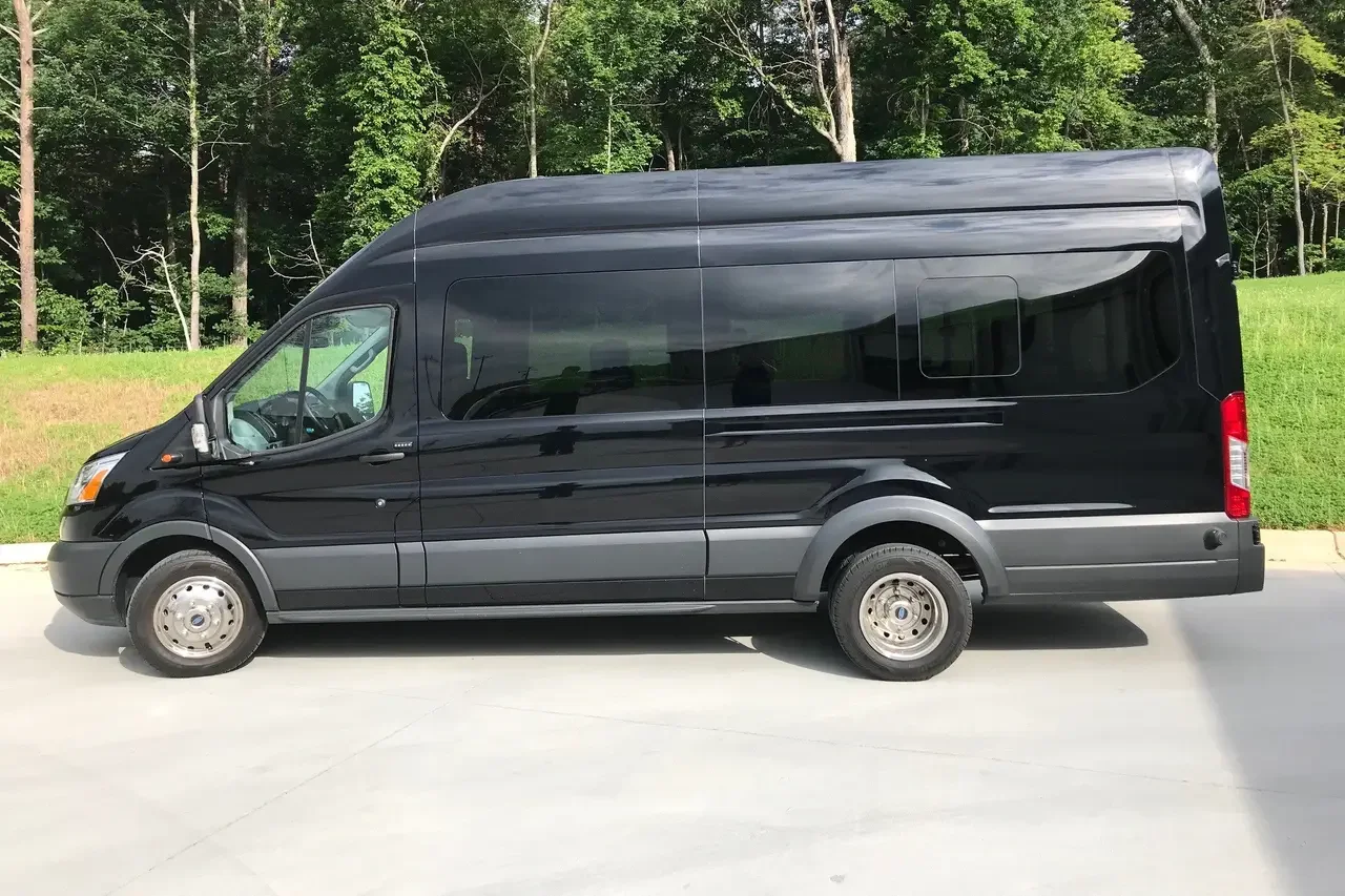 A black van parked on a concrete surface with a green grassy area and trees in the background.