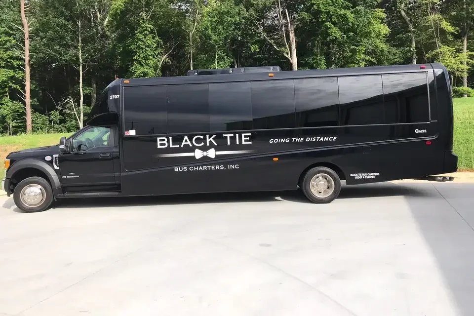 A black bus with the words 'BLACK TIE' and 'GOING THE DISTANCE' written on its side, parked on a paved area near green trees.