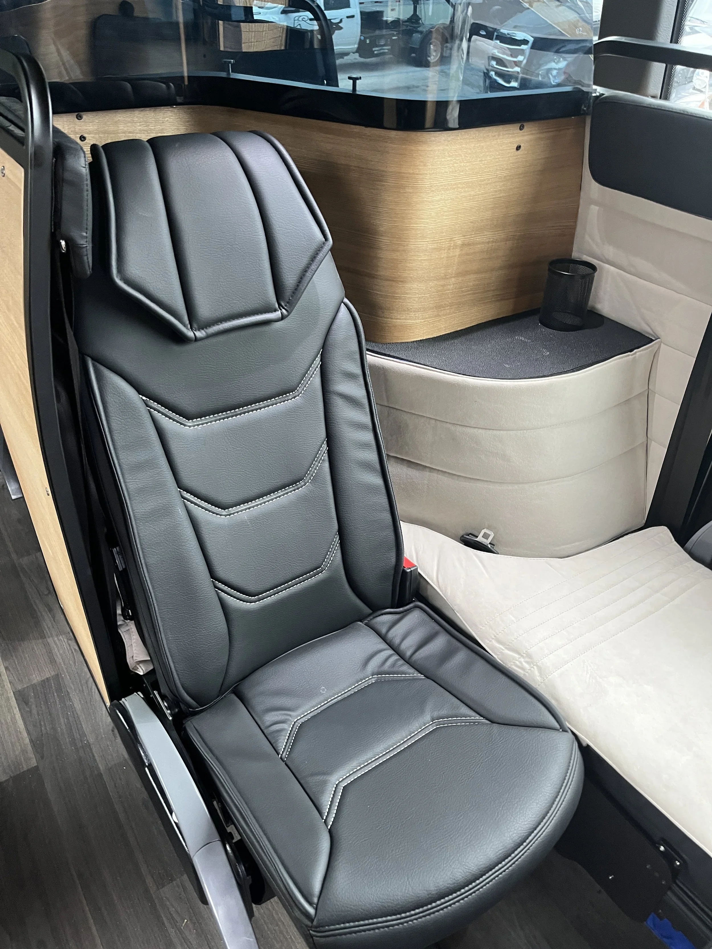 Interior of a vehicle with a black leather seat, a wooden panel, and a small cup holder on a beige padded surface.