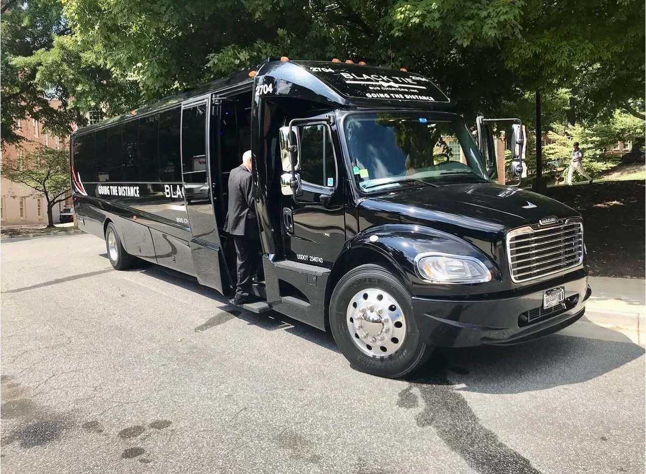 Black bus with the words 'Going the Distance' on the side and the front, parked on a street under trees, with a person opening the door.