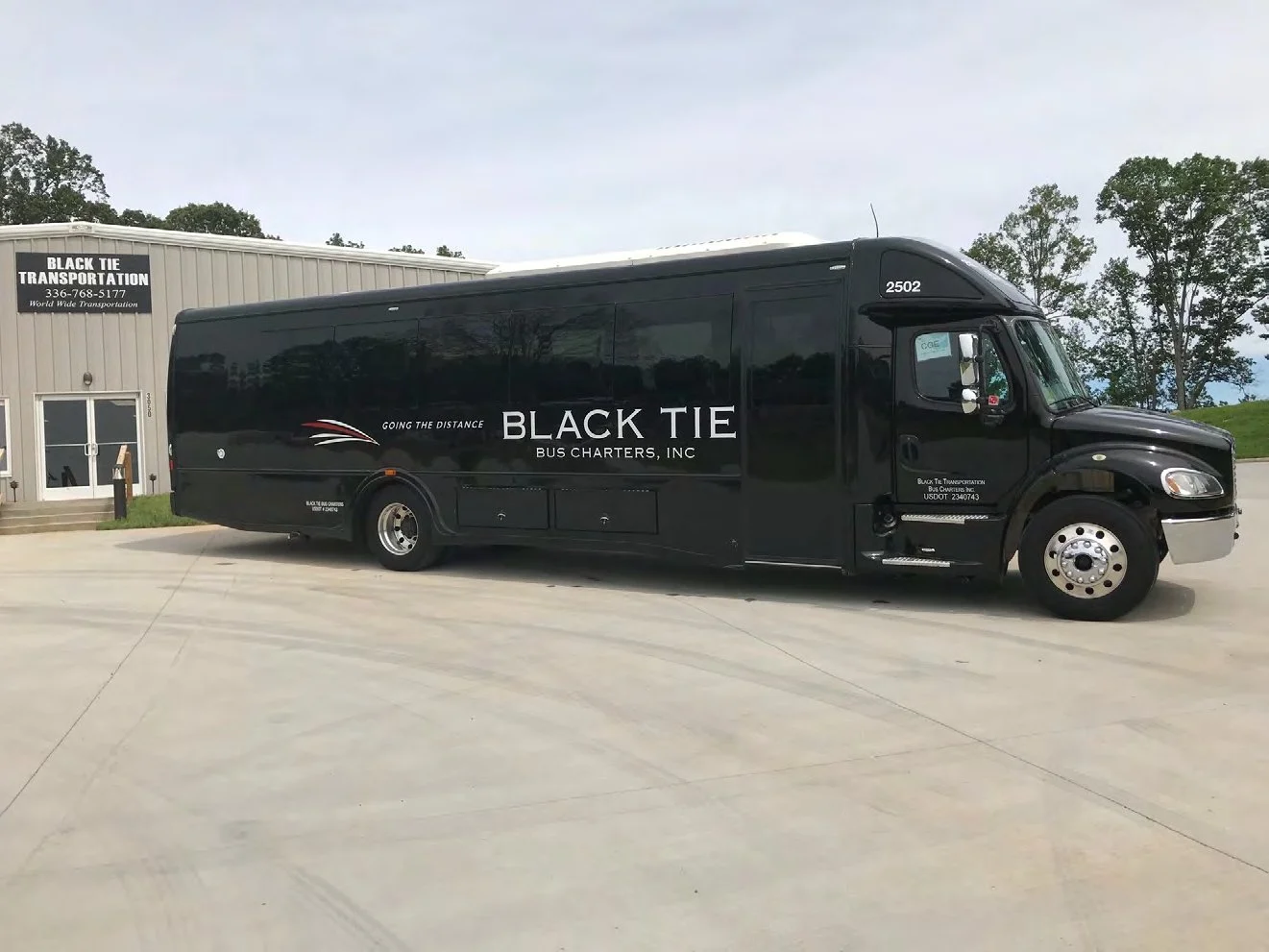 A black bus with the logo and text for Black Tie Bus Charters, Inc., parked outside a building with a sign for Black Tie Transportation, Inc.