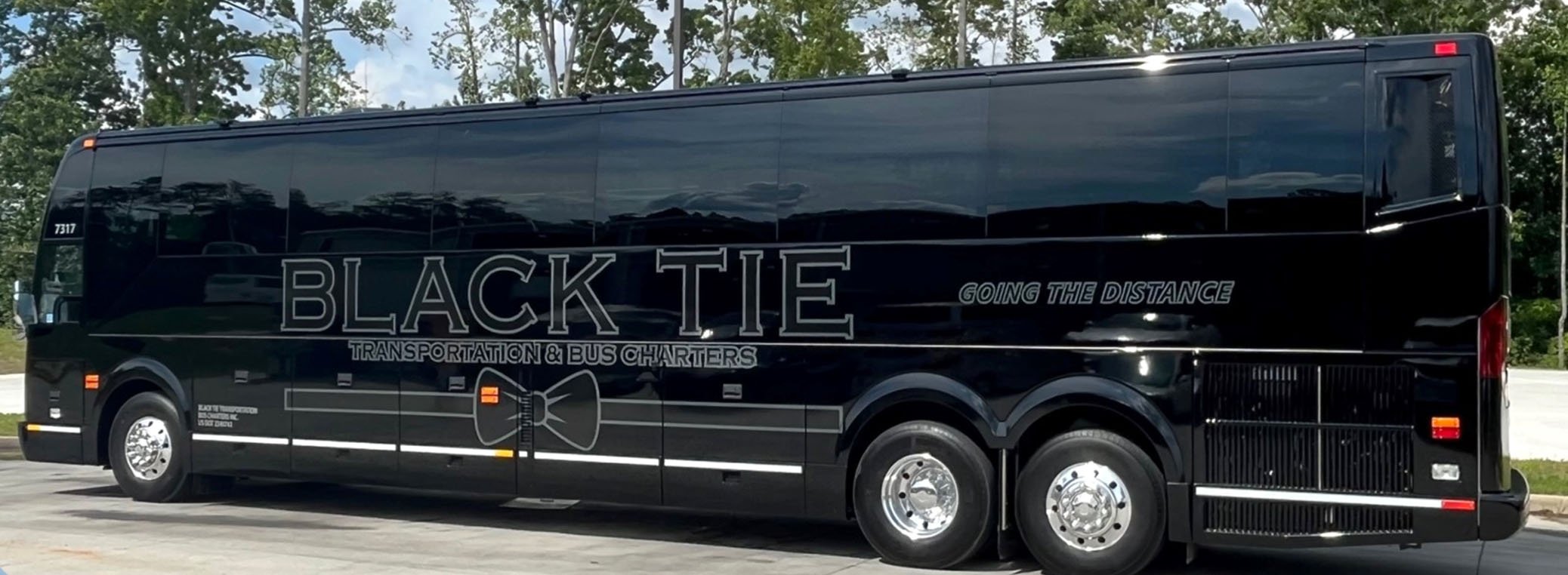 Black bus with company logo and slogan parked on road, surrounded by trees.