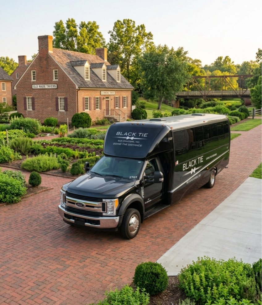 A black delivery van parked on a brick driveway in front of a brick house with a garden and trees in the background.