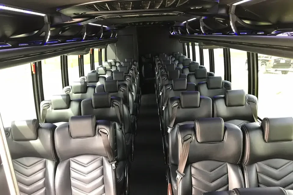 Interior of a bus with multiple rows of black leather seats, windows on both sides, and overhead storage compartments.