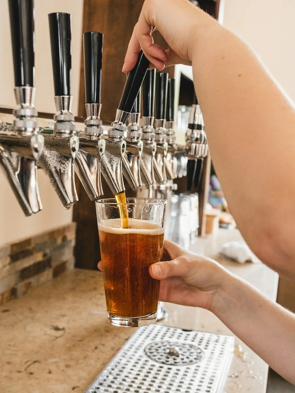 Person filling a glass with dark beer from a tap at a bar.