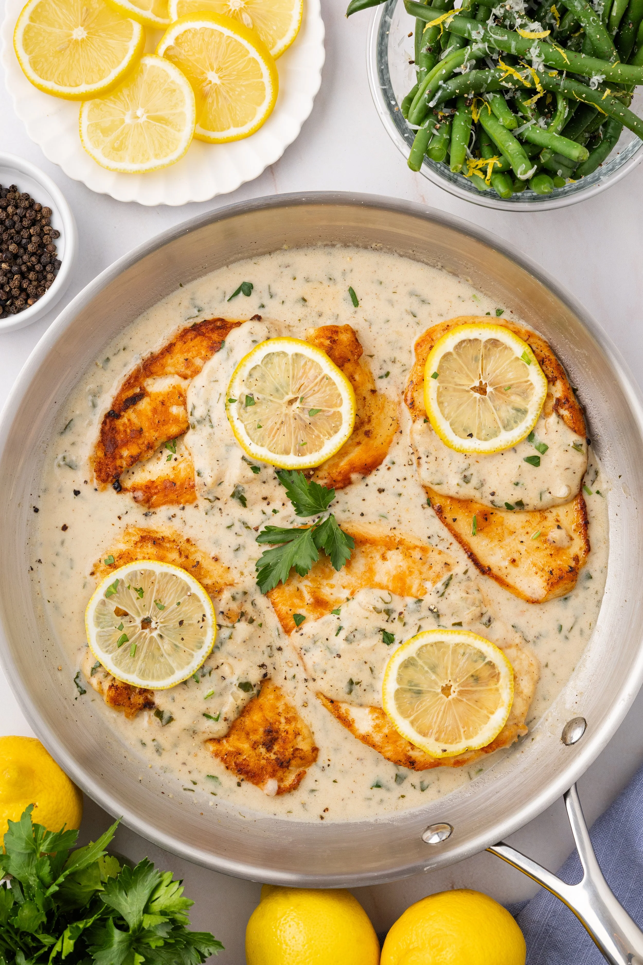 Chicken Breast in creamy lemon herb sauce, garnished with lemon slices and parsley, in a large skillet surrounded by fresh lemons and parsley.