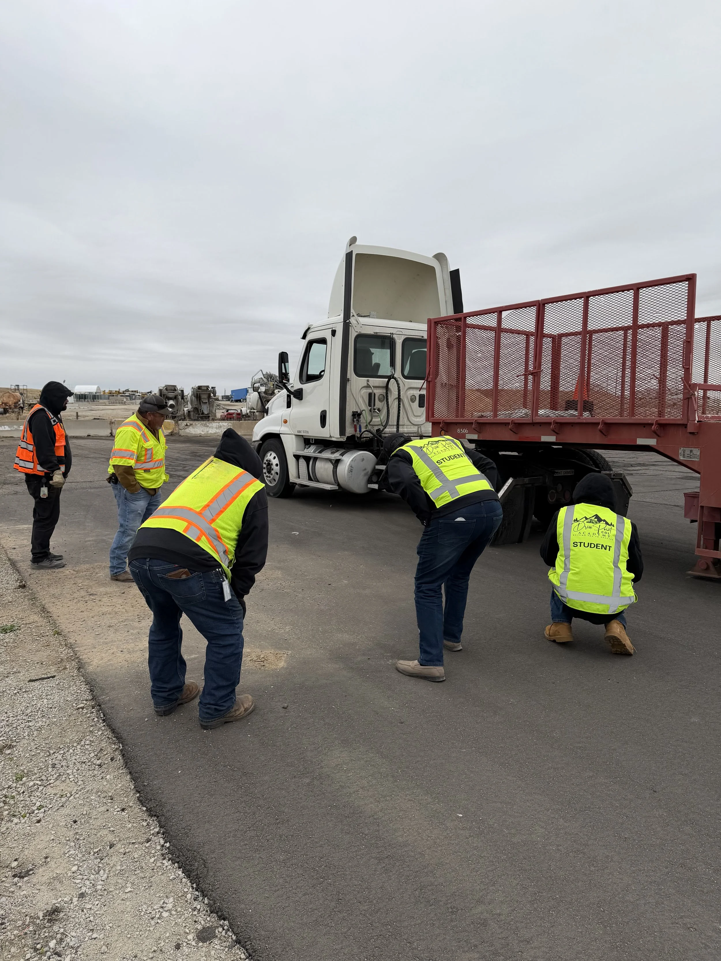 Several workers wearing high-visibility vests are learning how to connect and disconnect a semi truck.