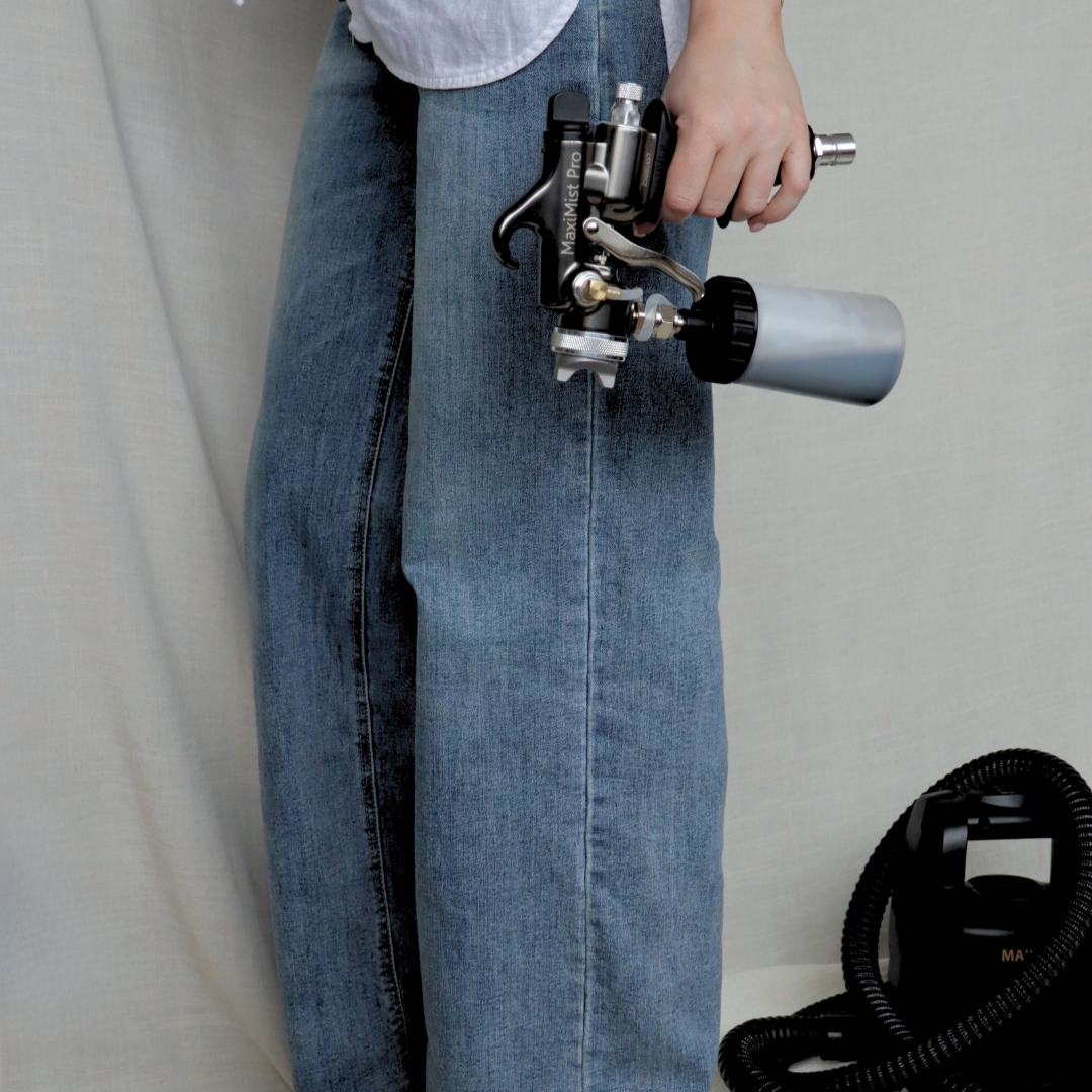 Person holding a paint spray gun while standing next to a black vacuum cleaner.