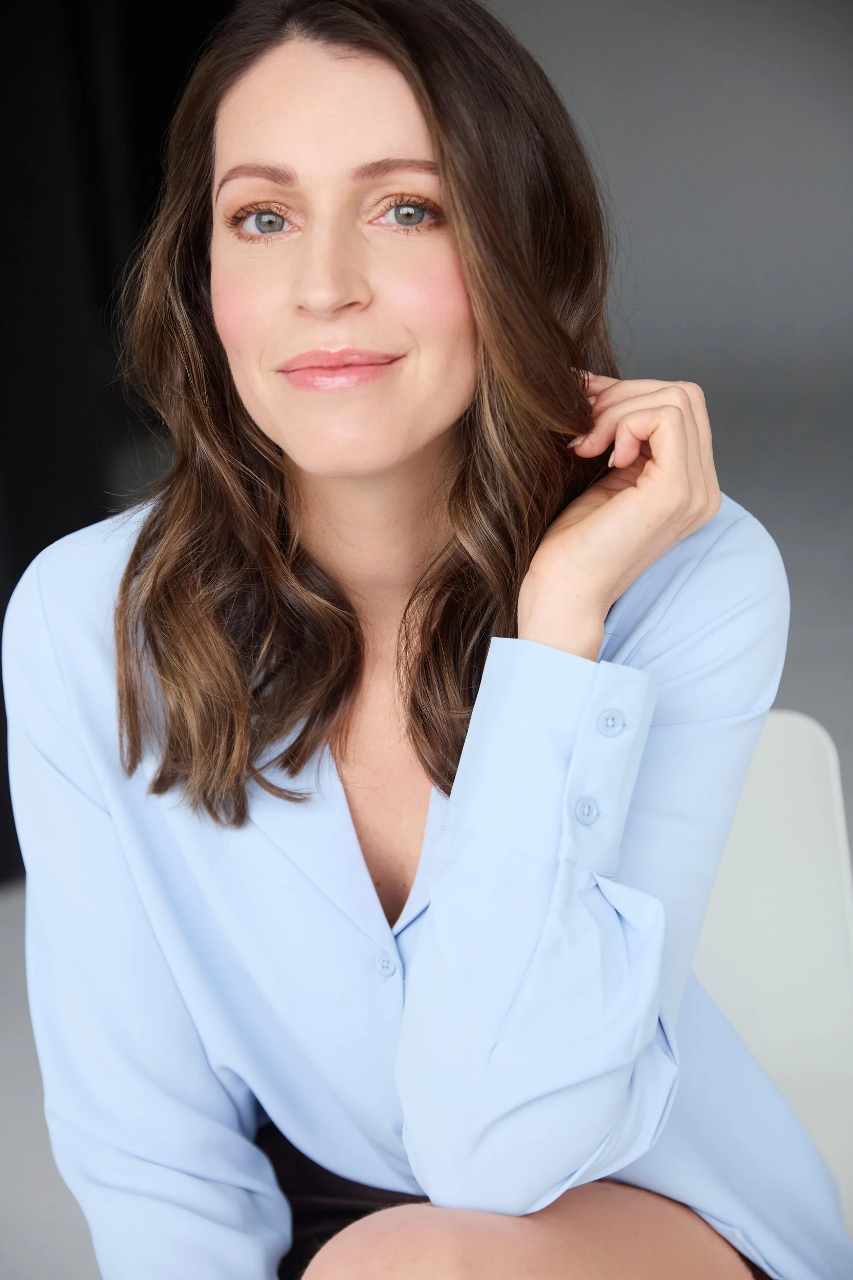 Une femme aux longs cheveux bruns et aux yeux bleus porte une chemise bleue claire et sourit doucement.