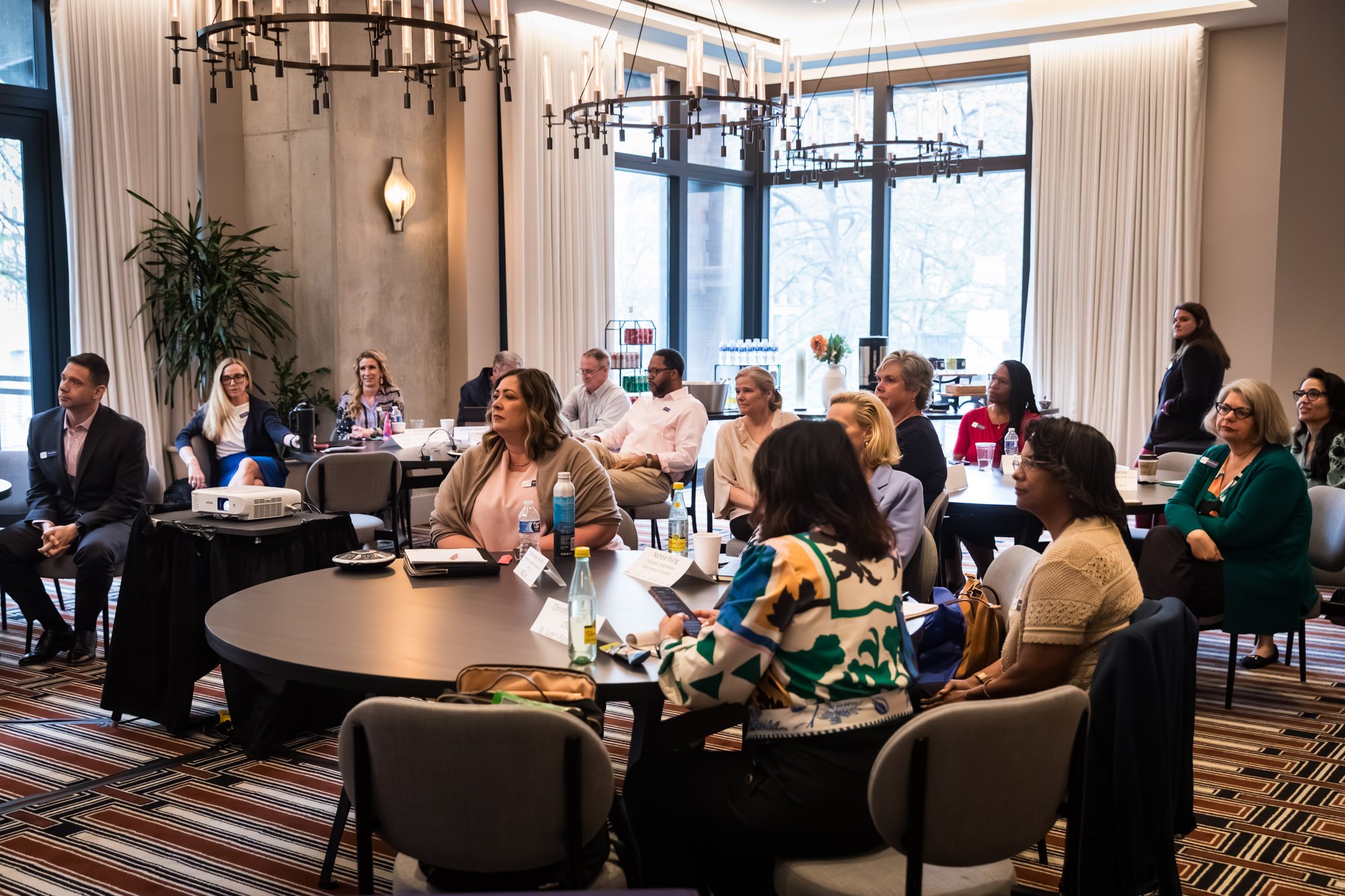 People seated around tables in a modern conference room, listening to a presentation about community-based family services
