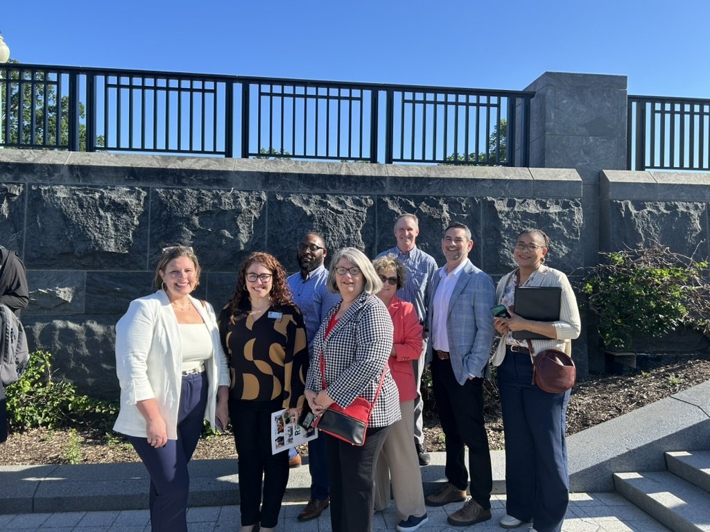 A group of nine adults for  child and family services, standing outdoors on a paved area in front of a stone wall, smiling at the camera.