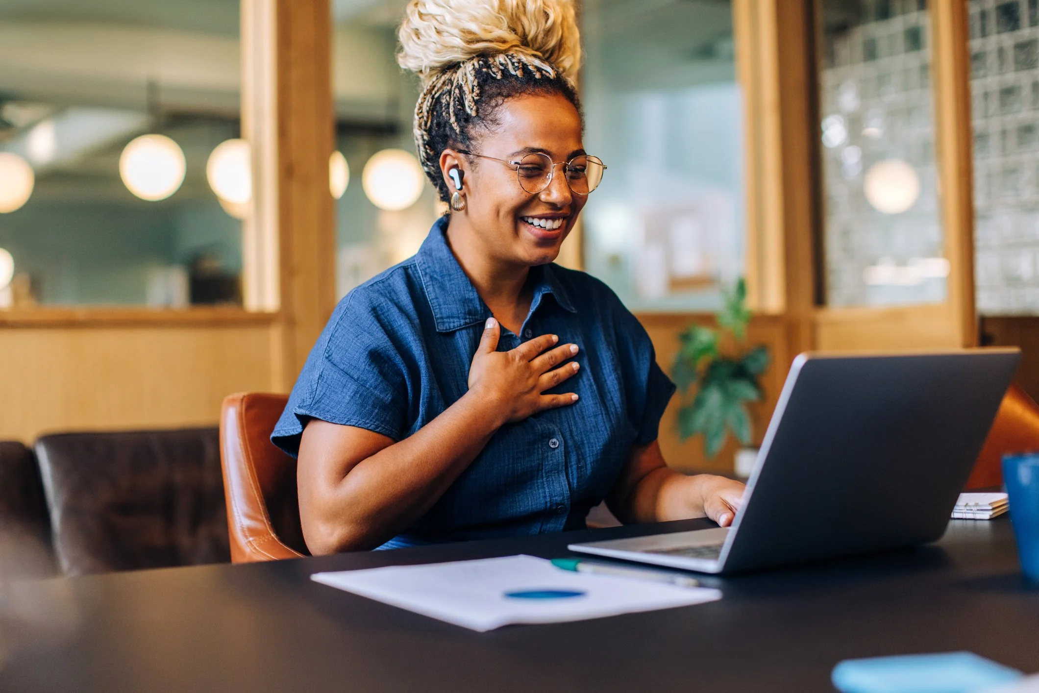Person wearing headphones smiles and gestures while participating in a video call at a desk about kinship care resources.
