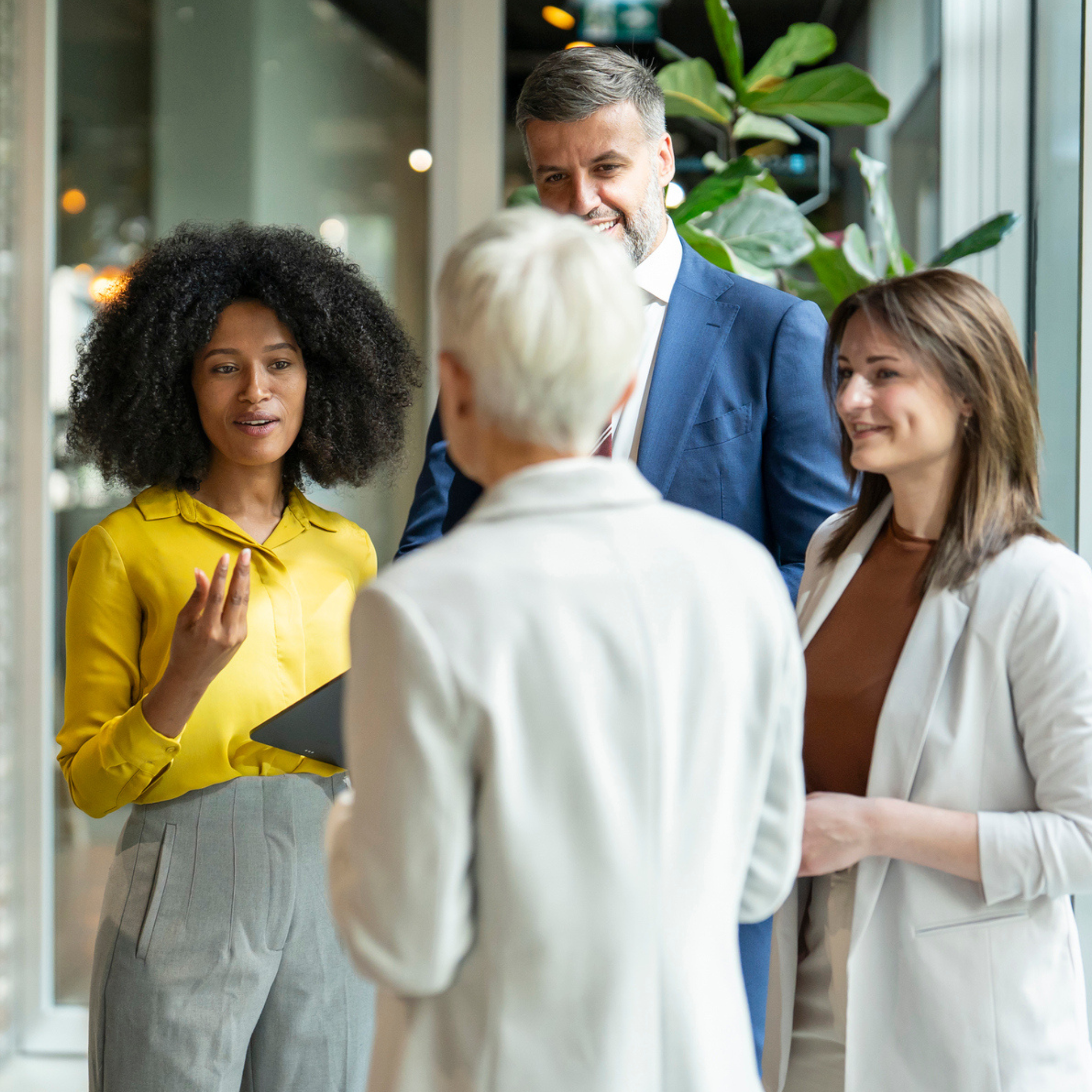 Four people in business attire stand indoors, engaged in conversation about connection, education and advocacy.