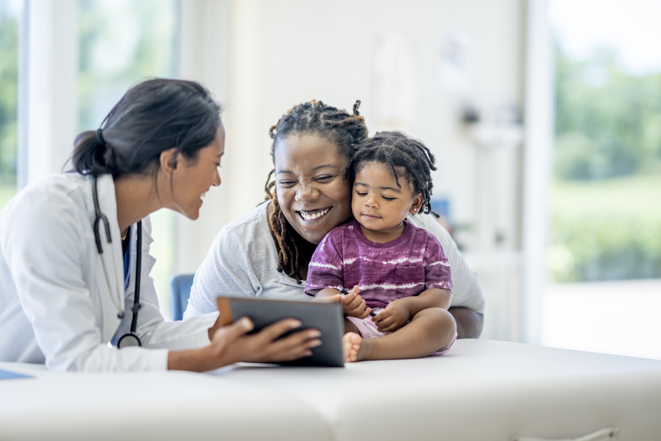 A doctor talking to a woman and a young girl in a medical office, with the woman smiling and the girl looking calm.