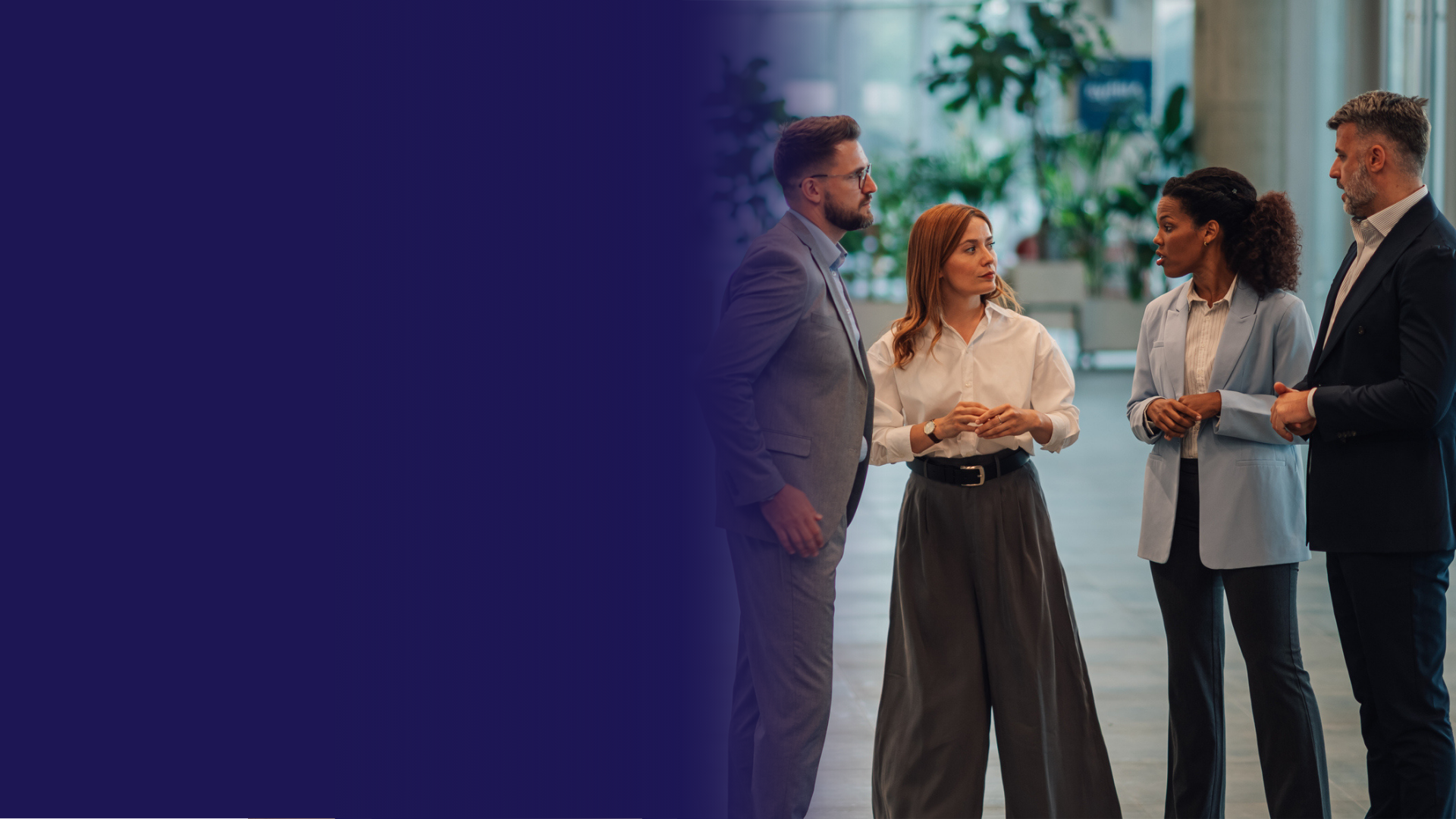 Four business professionals stand and talk in a modern office space with plants in the background discussing family focused treatment.