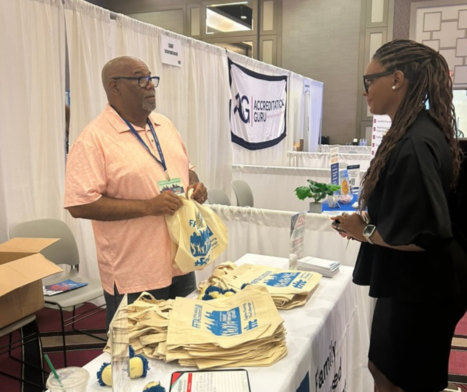 A man and a woman talk at an exhibit booth for FFTA with promotional tote bags and brochures displayed on the table.