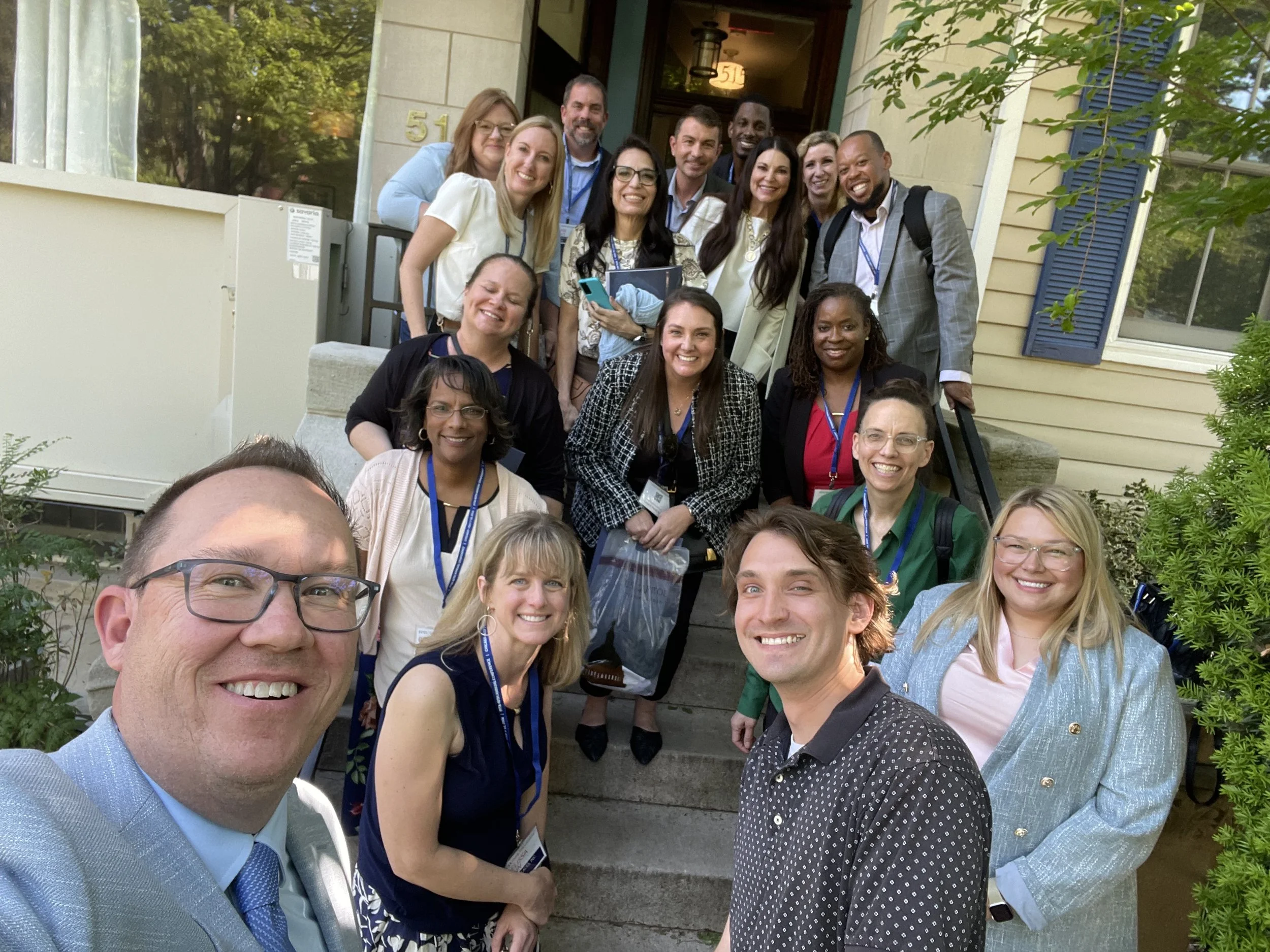 A group of family services professionals pose and smile for a photo on the steps outside a house on a sunny day.