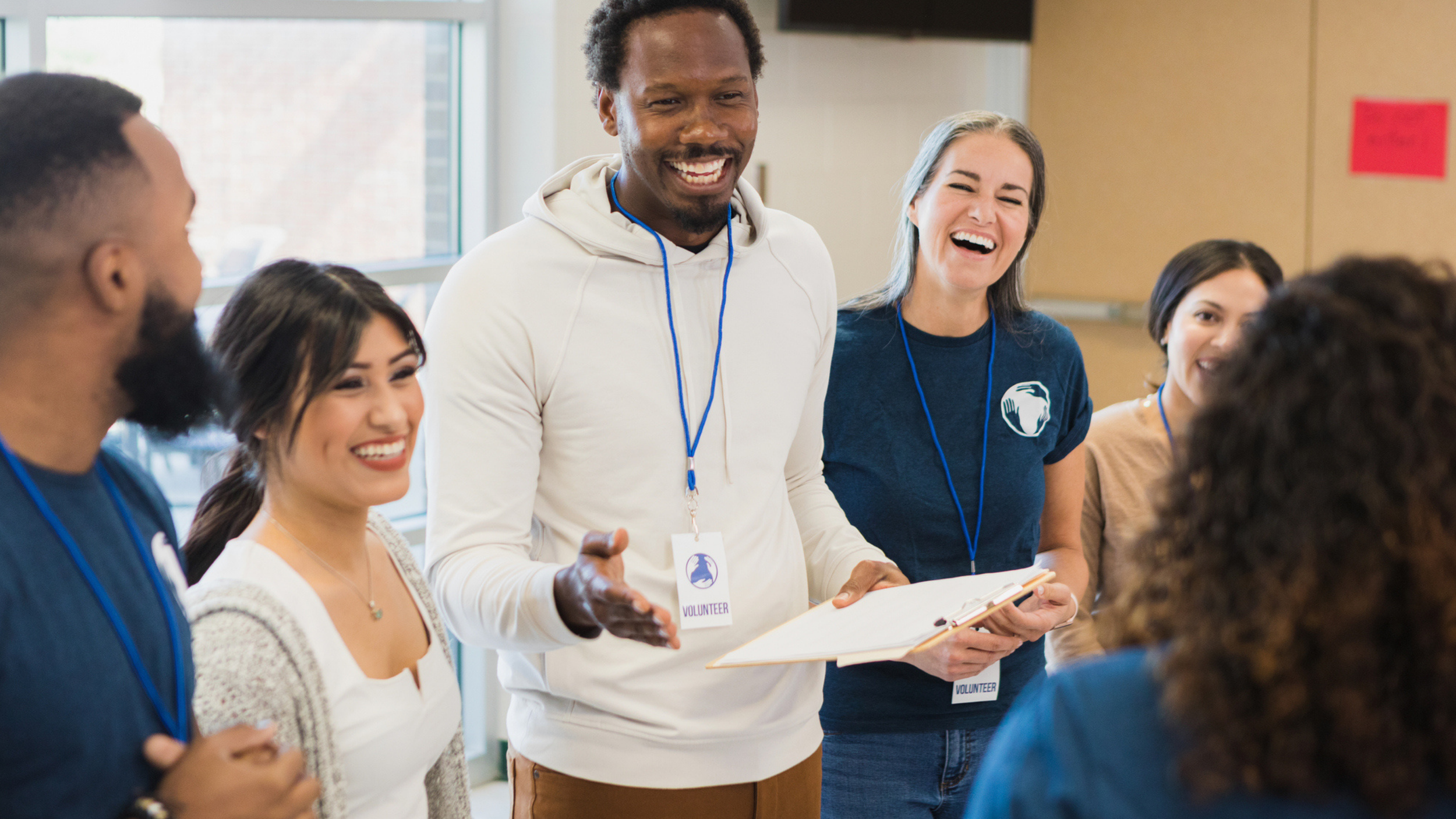 A group of adults wearing name badges stands in a circle indoors, smiling and laughing together talking about FFTA, a human services association
