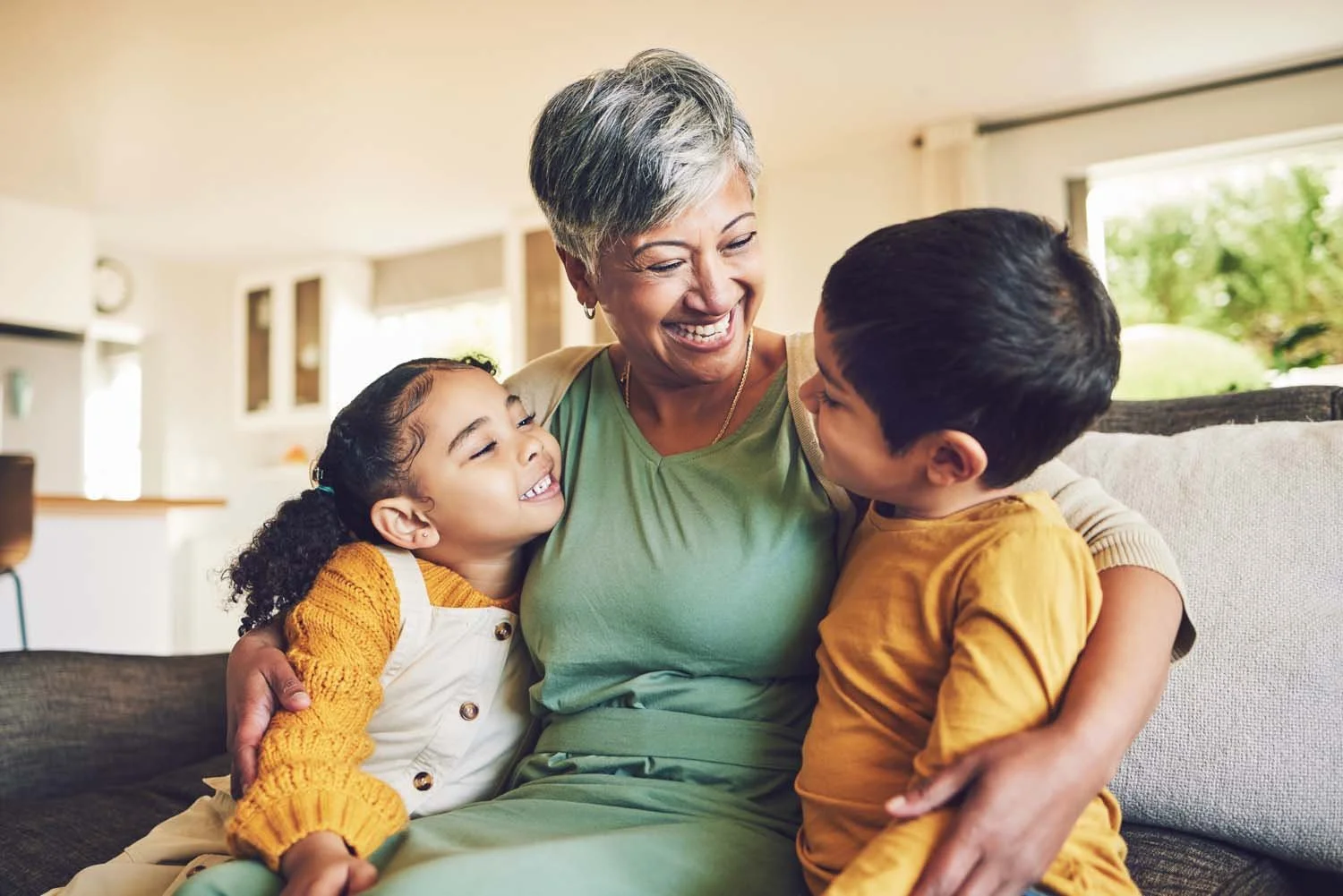 Older woman sitting on a couch, smiling and hugging two young children showcasing family based treatment care.