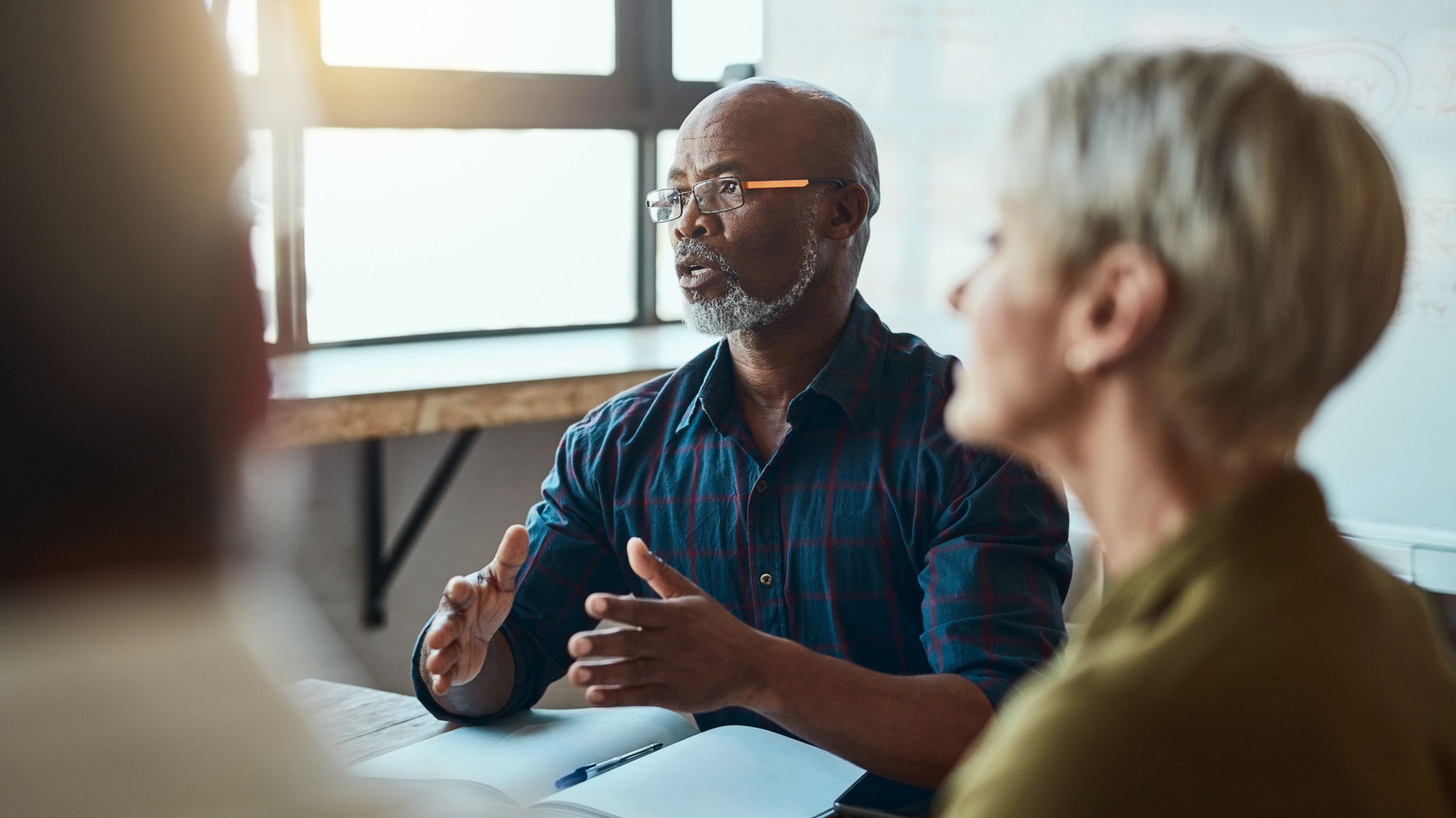 Man speaking about behavioral health organizations seated at a table with two other people, with a notebook open in front of him.
