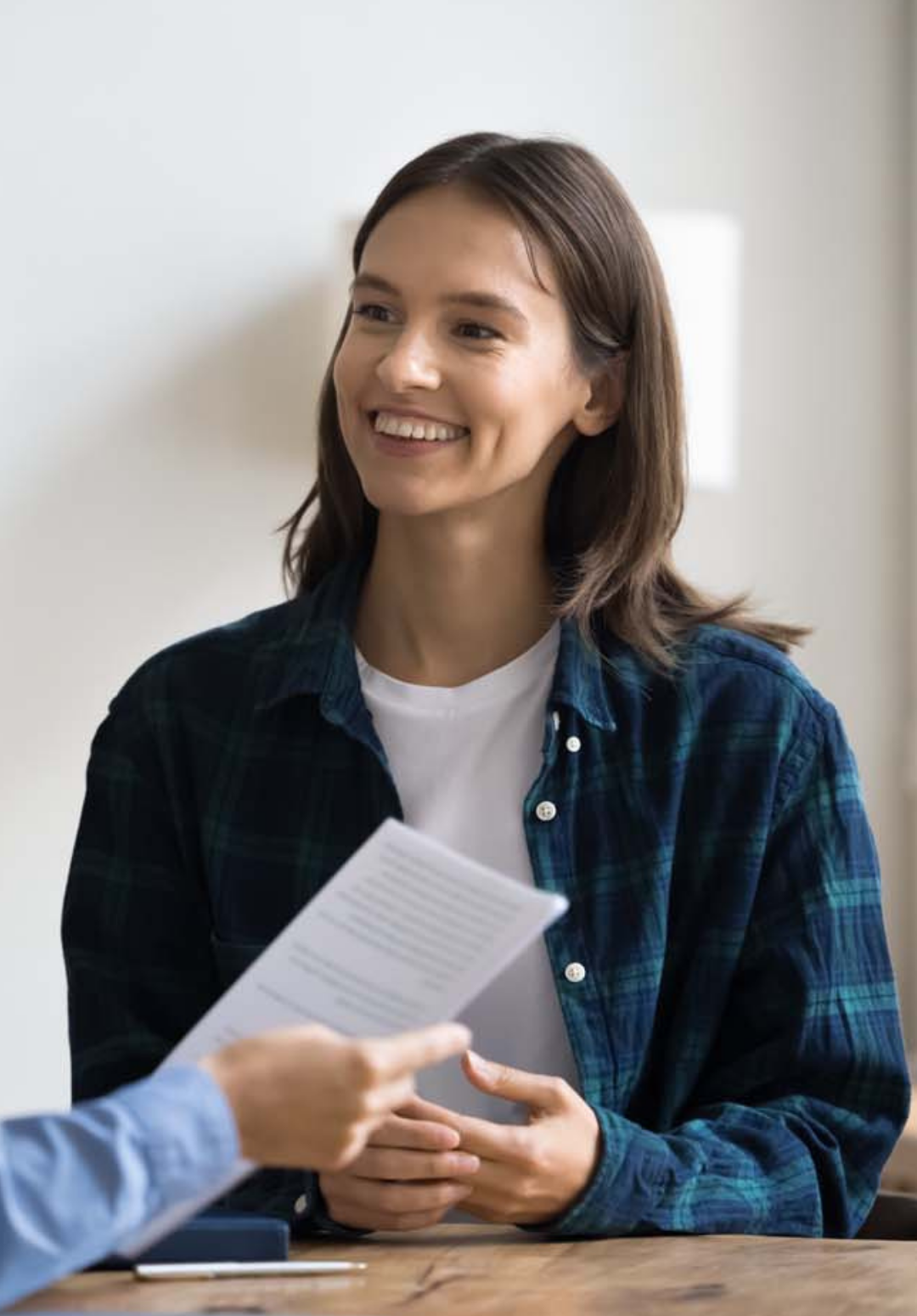 Smiling woman in a plaid shirt sits at a table, listening to someone talk about child and family services.