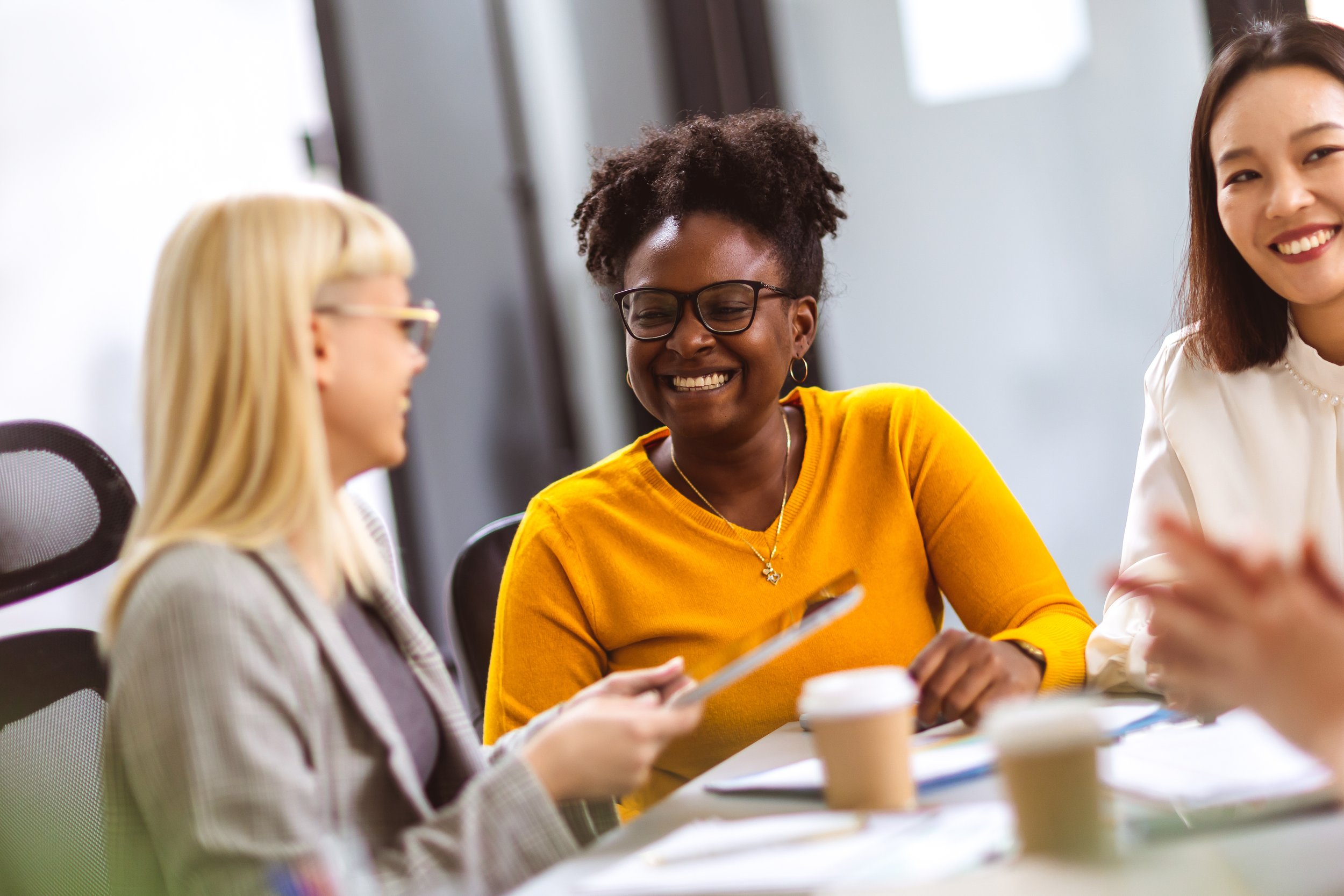 Three people sit at a table in an office, smiling and talking about child welfare organizations with papers and coffee cups in front of them.