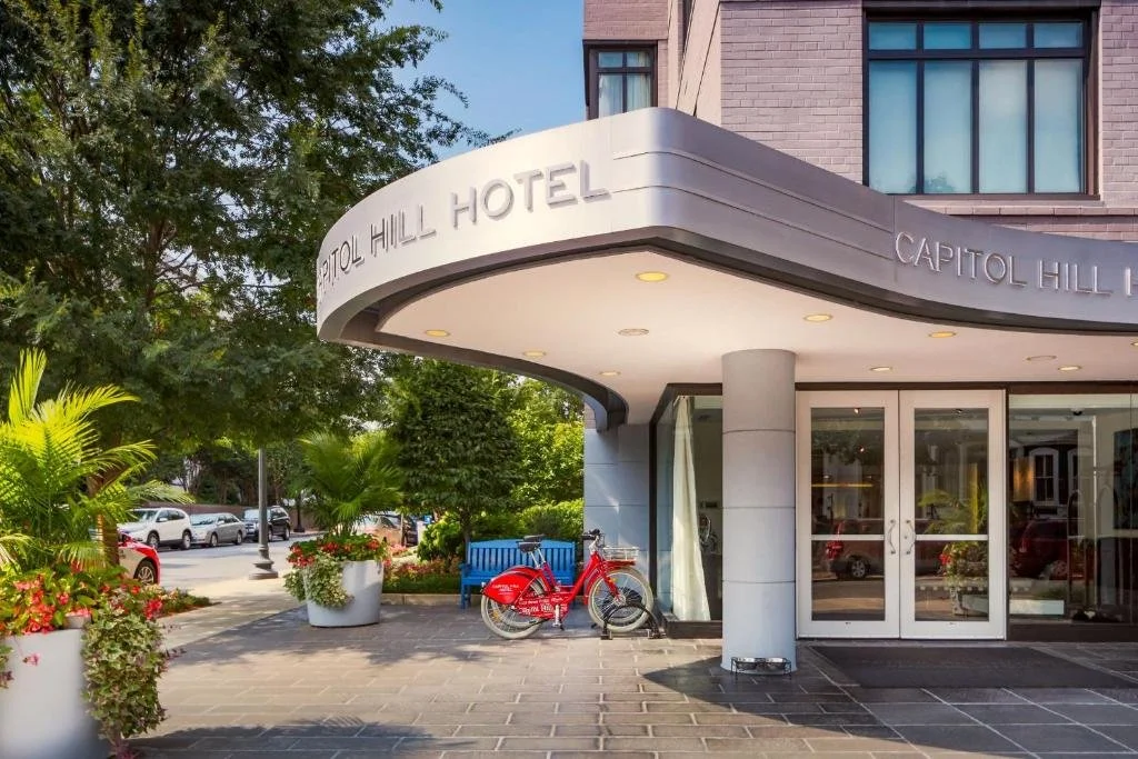 Exterior view of the Capitol Hill Hotel entrance with potted plants, a red bike, and parked cars on the street to show FFTA Public Policy Institute.