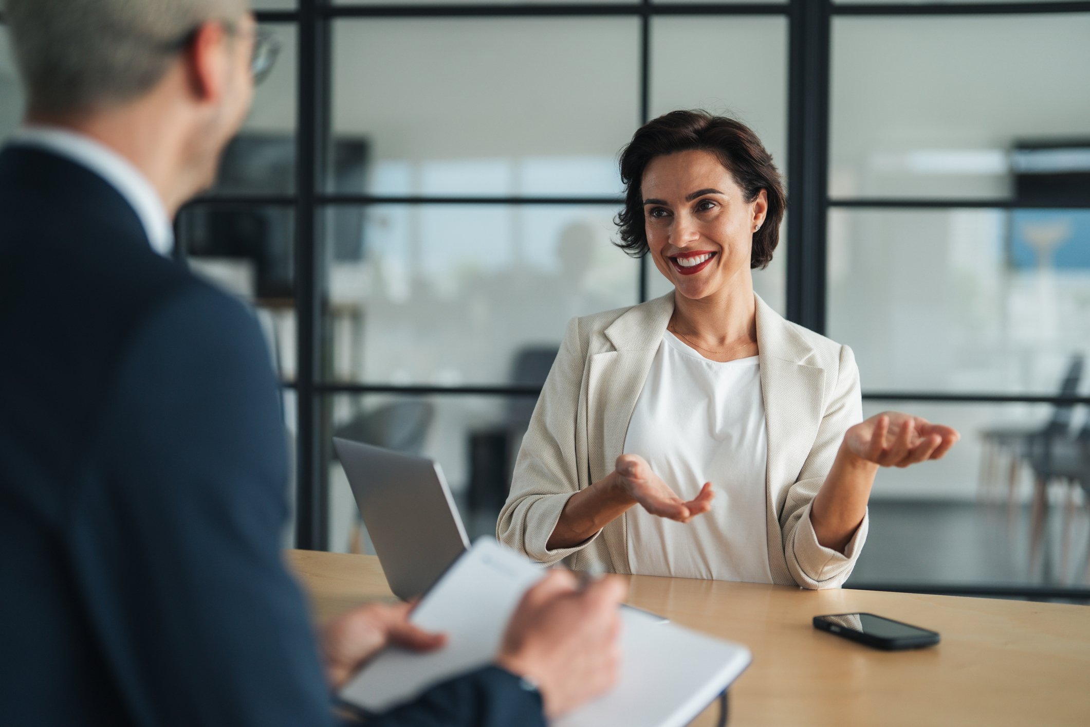 Woman in business attire speaks and gestures during a meeting as another person takes notes across the table about family support services