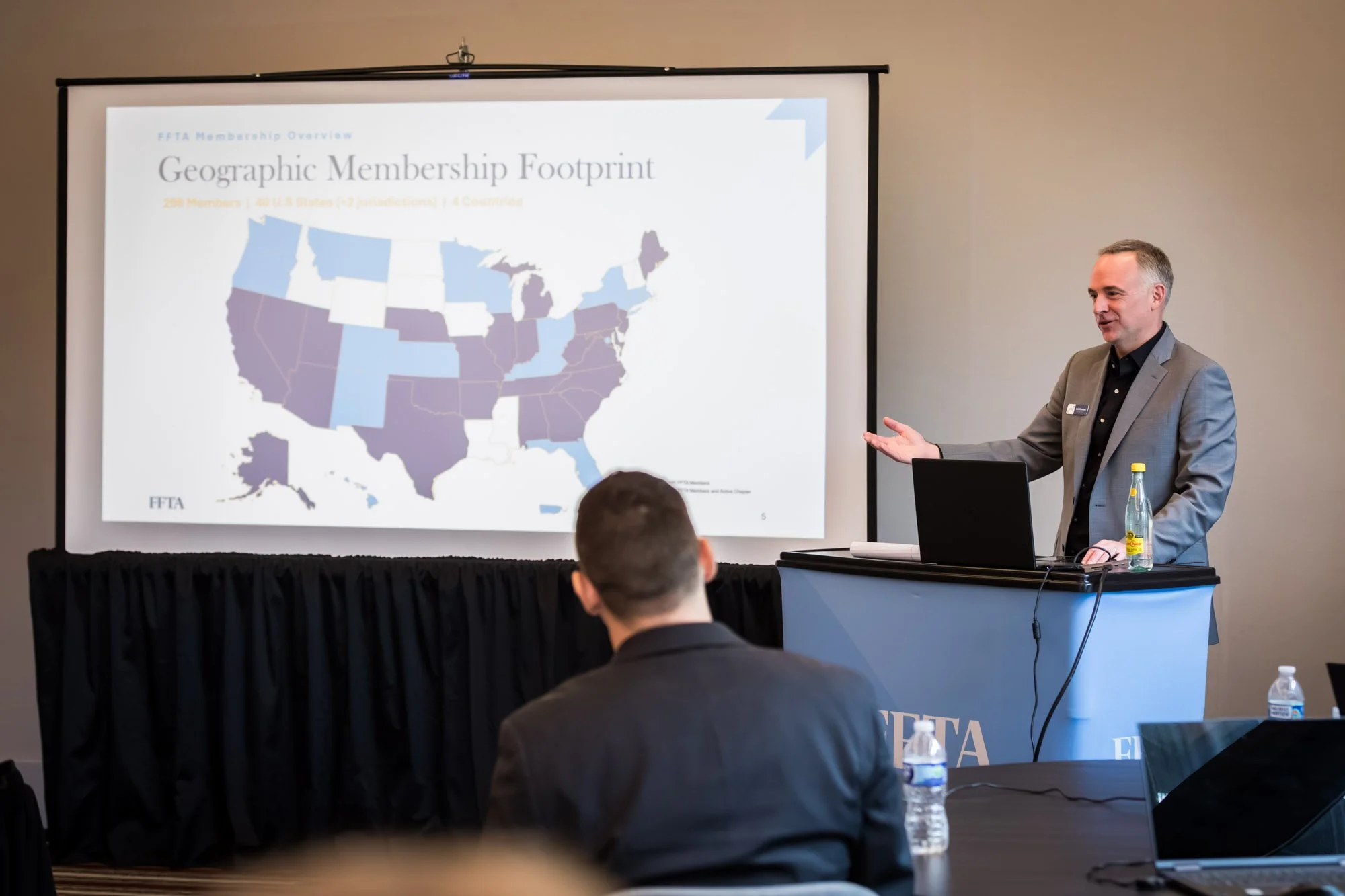 A man presents a slideshow about geographic membership footprint to an audience of family support services in a conference room.
