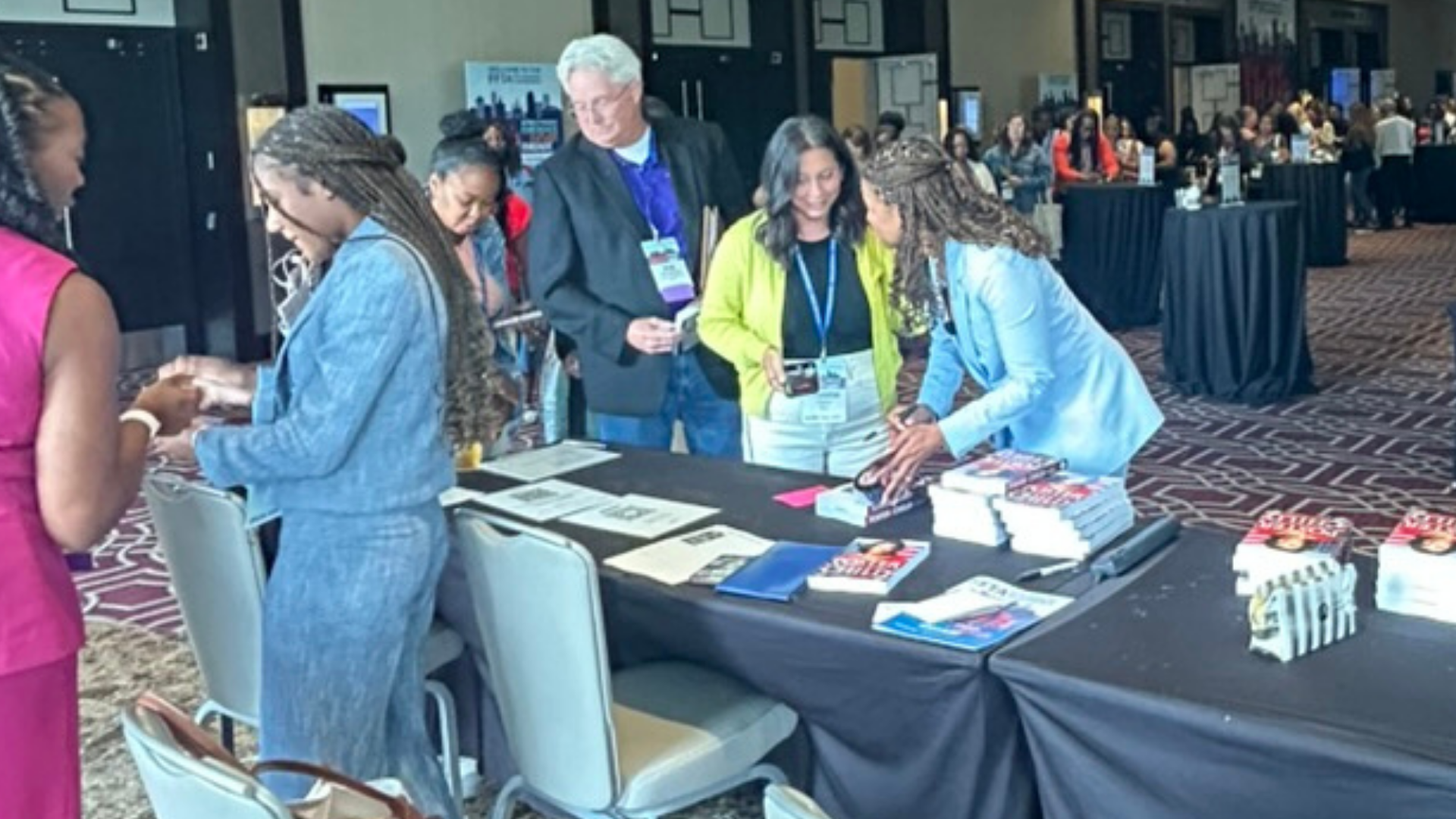 People interacting at a FFTA conference registration table with books, brochures, and name tags displayed.