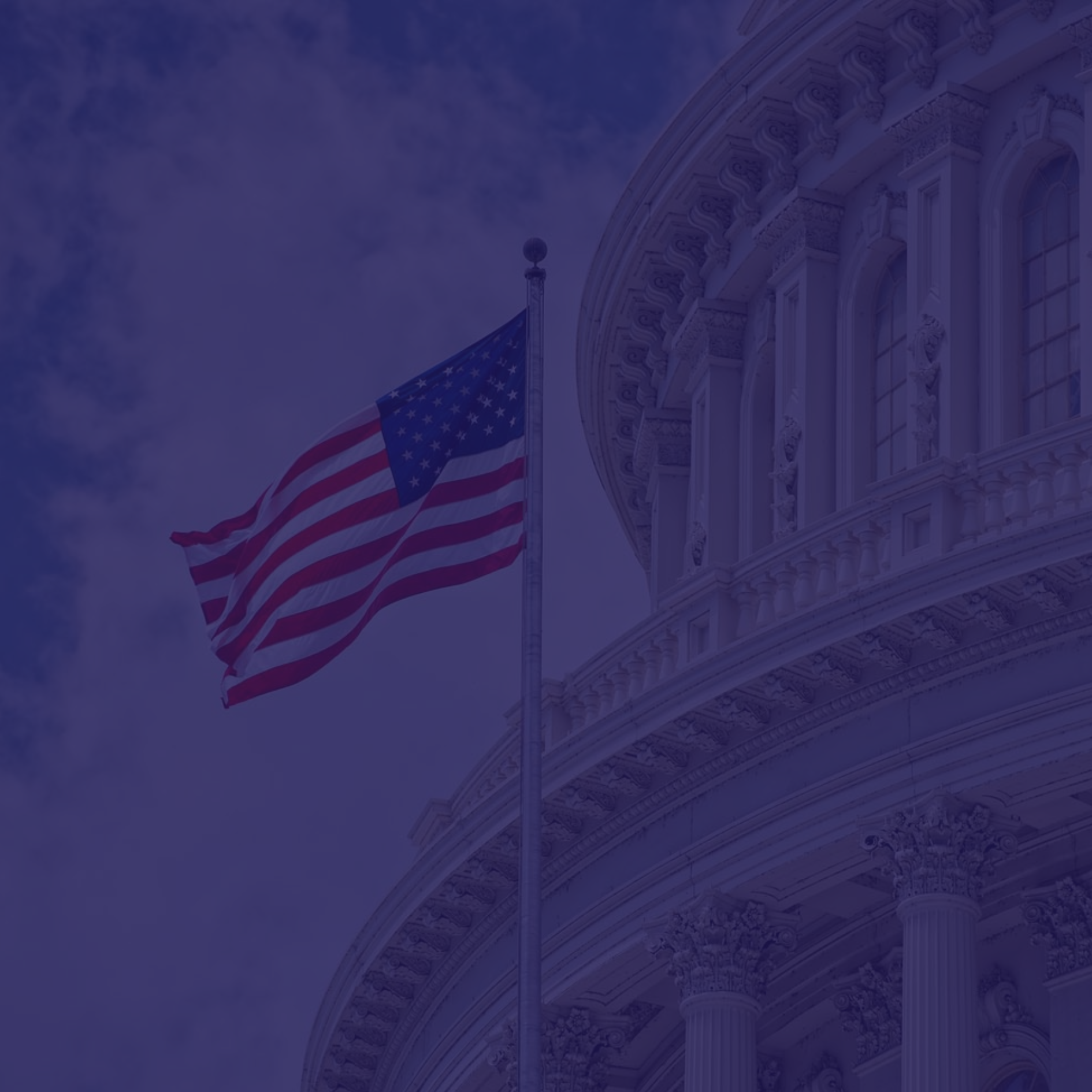 An American flag on a flagpole waves in front of a government building with columns and ornate architectural details.