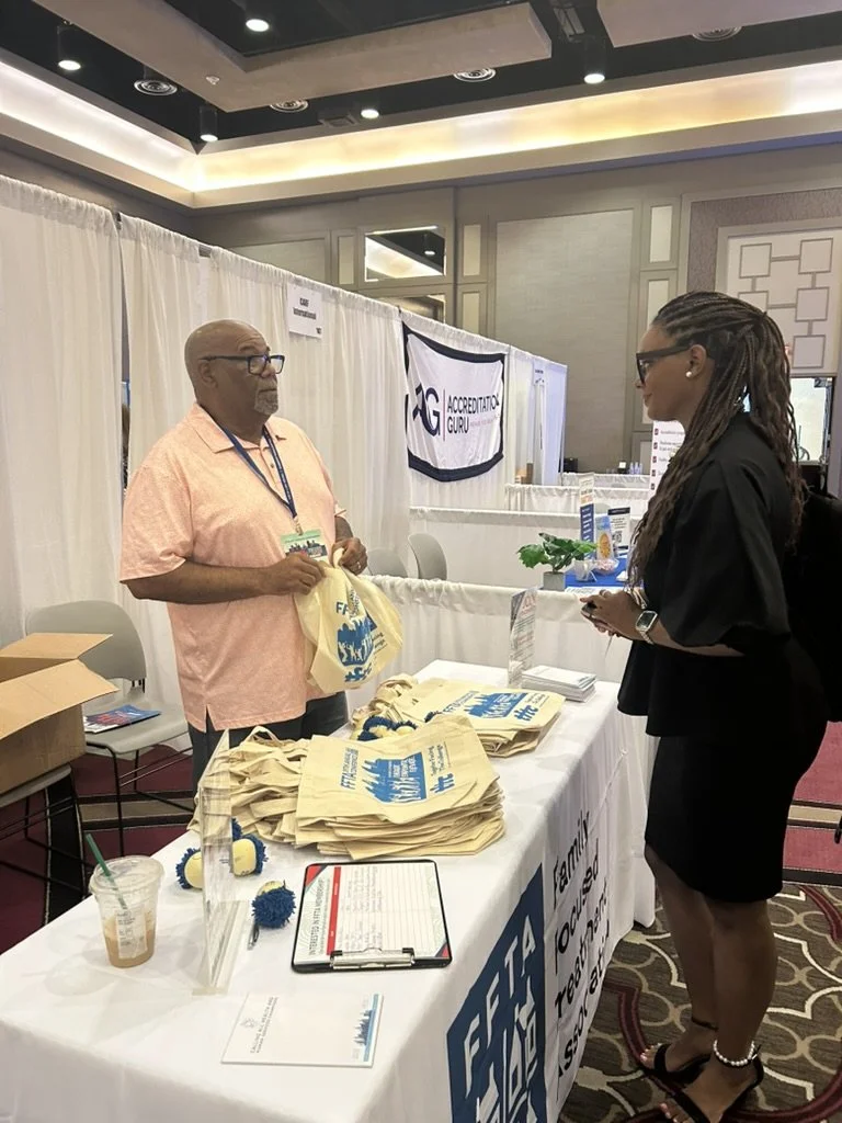 A man and a woman talk about family support services at an informational booth with tote bags and flyers at a conference or expo.