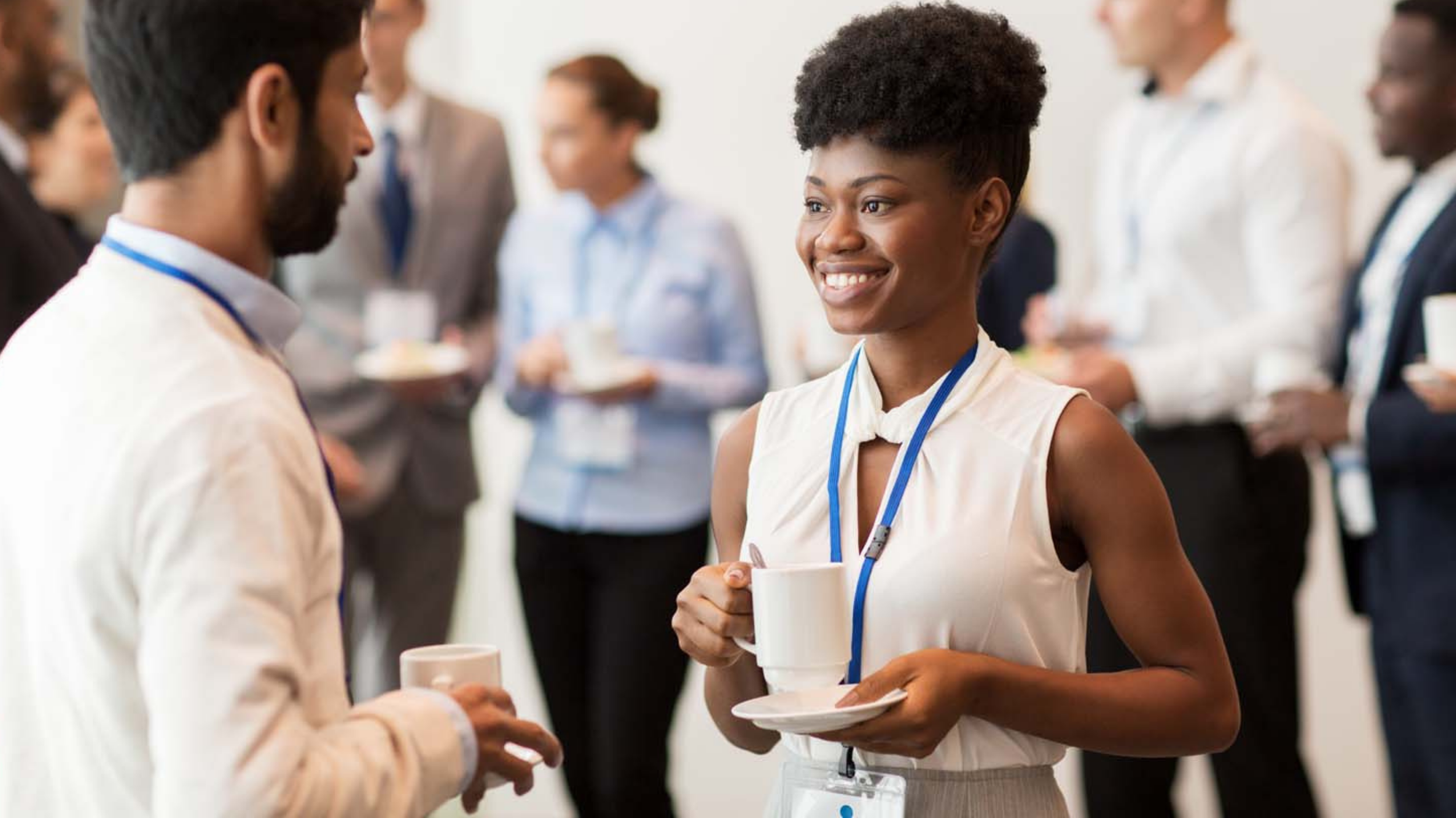 People wearing name badges talk about Community-based family services and hold coffee cups at a professional networking event or conference