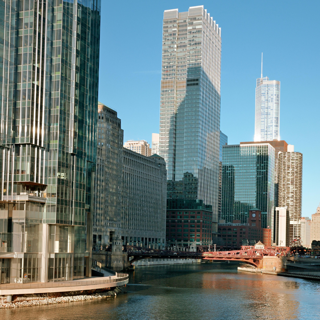 A view of tall modern skyscrapers along the Chicago River with a bridge in the foreground under a clear blue sky for human services organizations