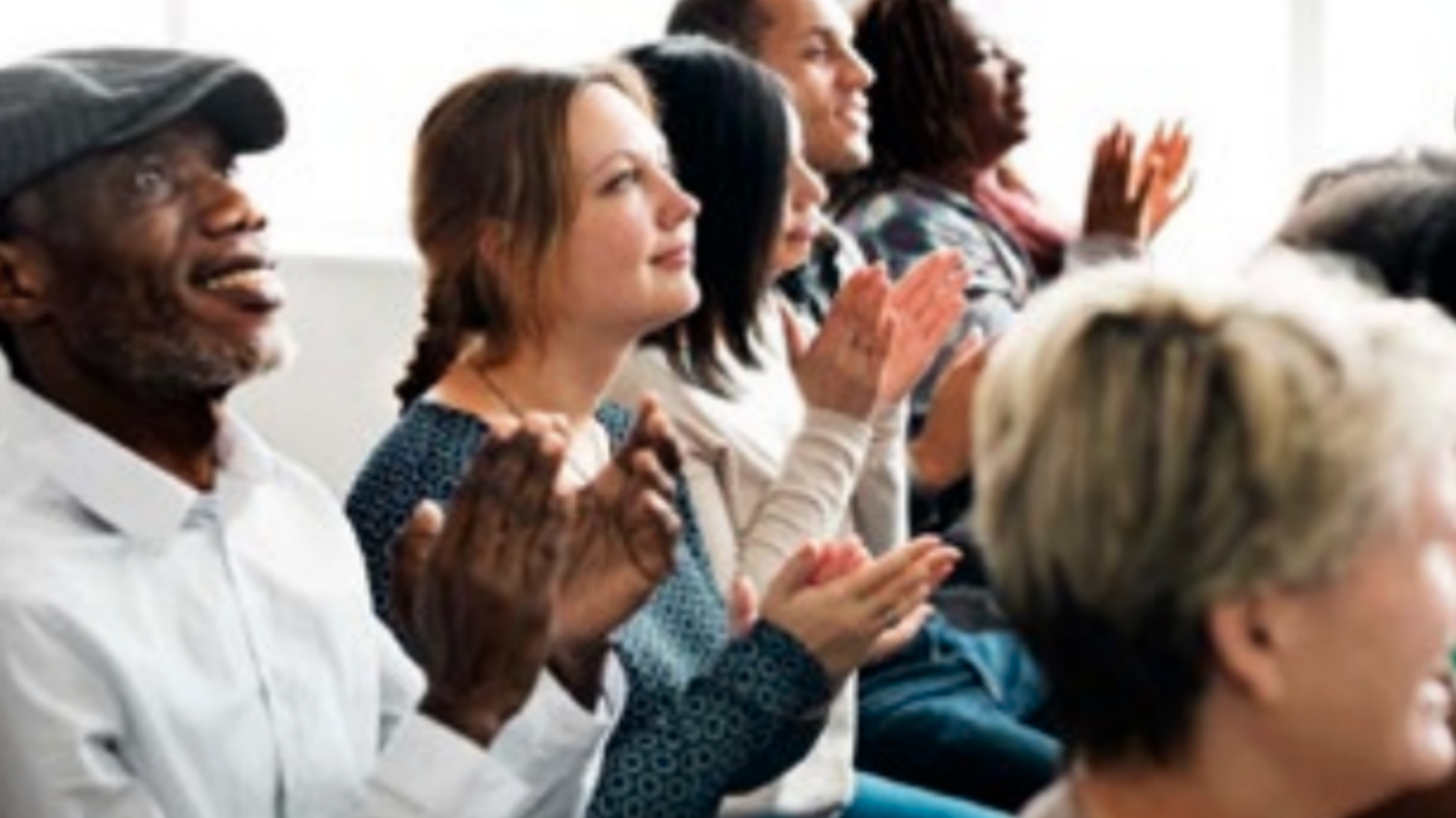 A group of people sitting in rows and clapping, appearing to watch or listen to a presentation about human services association.