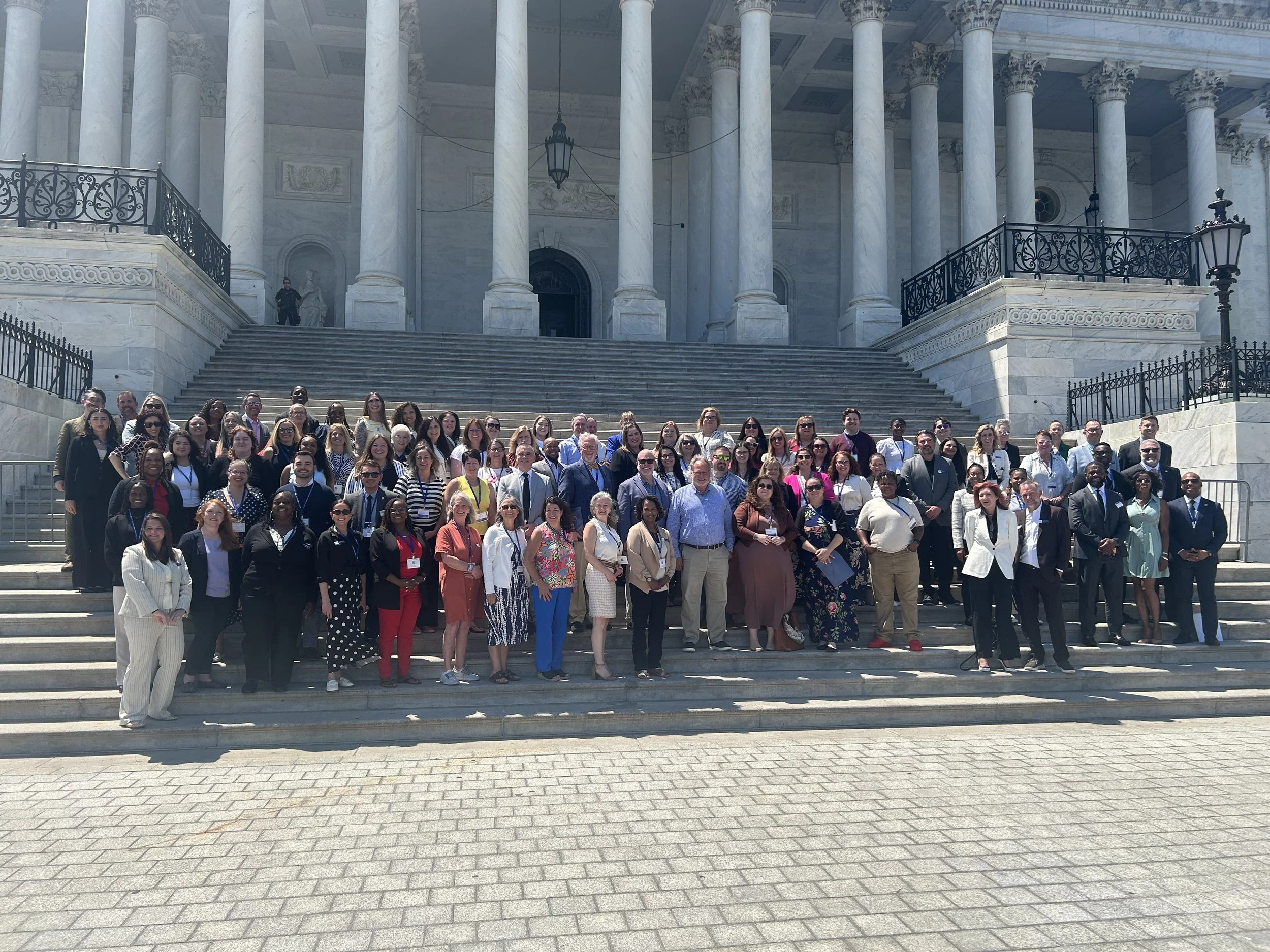 A large group of people apart of FFTA, pose for a photo on the steps outside a white marble building with columns.