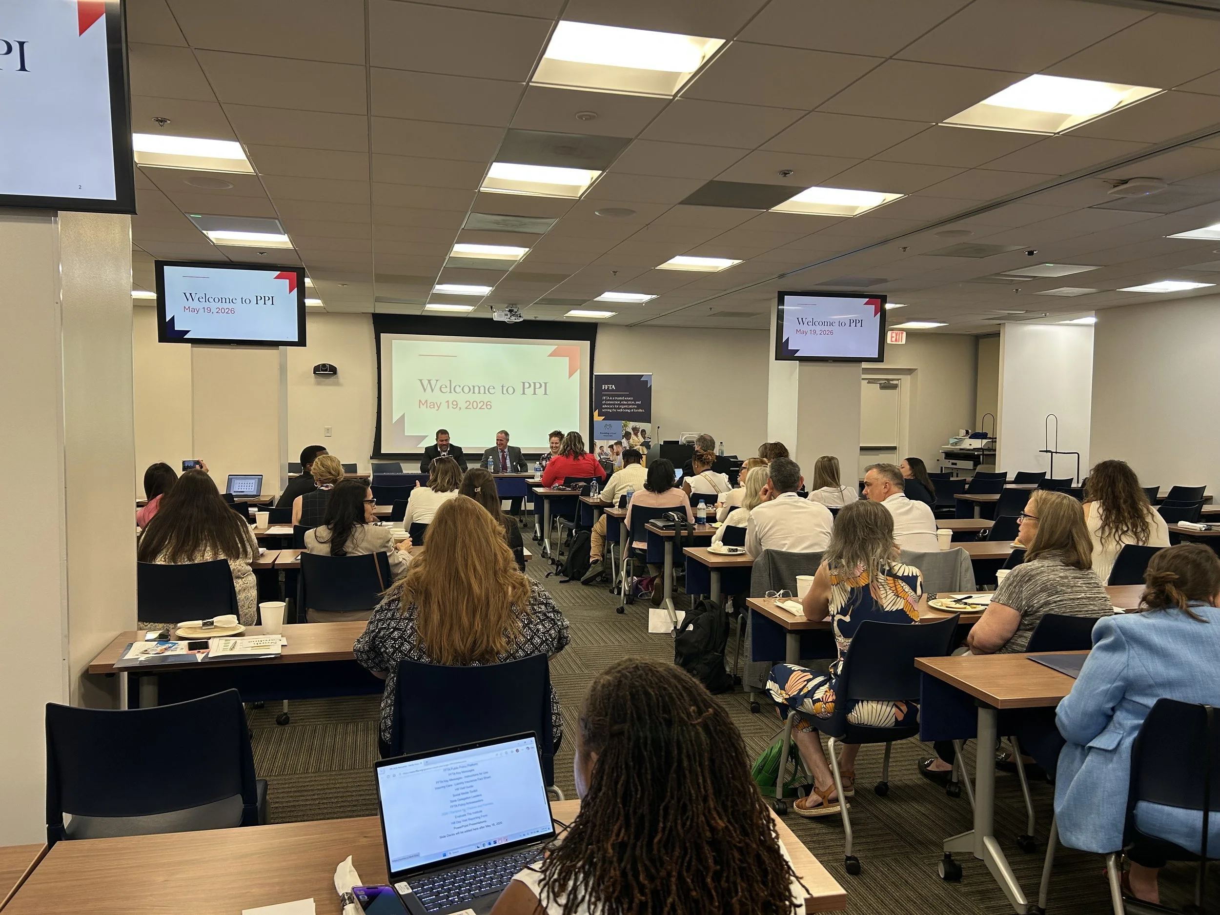 People sit in a conference room facing a screen that reads "Welcome to PPI, May 19, 2023" during a human services association meeting.
