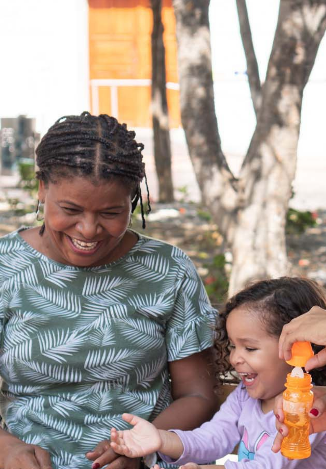 An adult and a child sit outdoors, smiling together while the child plays with a bottle of bubble solution representing child welfare association.