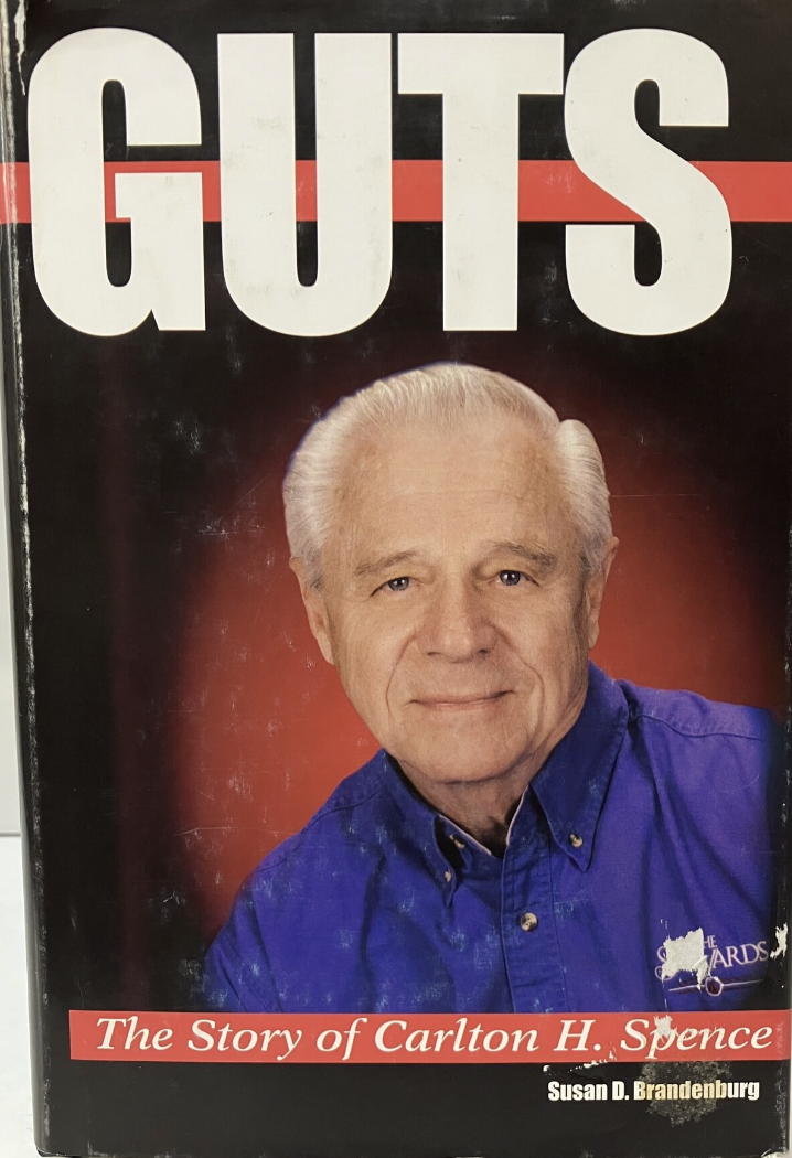 Book cover titled "GUTS" with a photo of an older man with white hair wearing a blue collared shirt. The subtitle reads "The Story of Carlton H. Spence" by Susan D. Brandenburg.