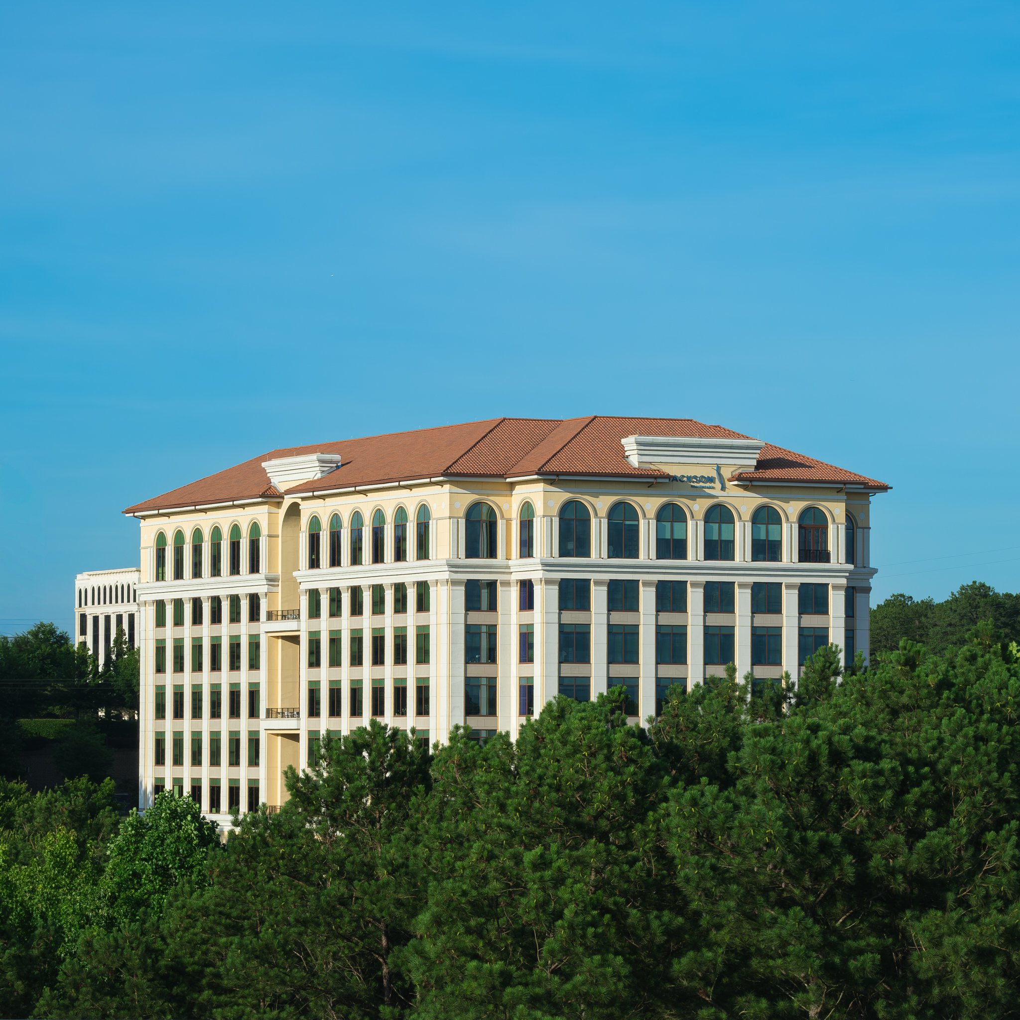 A tall building with arched windows on top floors and columns at the base, bathed in warm sunlight. | Real Estate Photography | Alpharetta | Milton | Buckhead | Atlanta | Drone | Video | Luxury | Jackson Healthcare | Rick Jackson | Mayor | Architectu