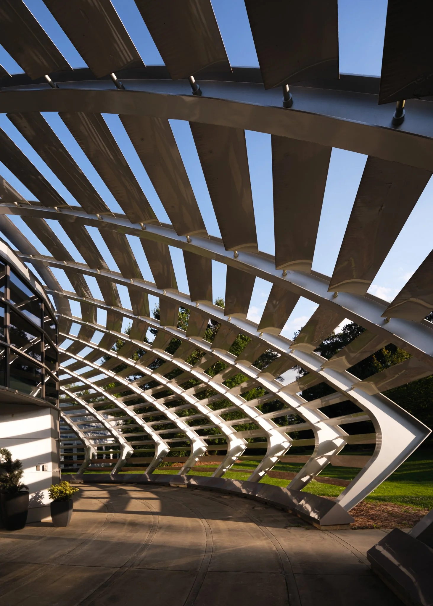 Modern building with a curved metal and glass roof in front of a green lawn and trees, under a clear sky at sunset. | Real Estate Photography | Alpharetta | Milton | Buckhead | Atlanta | Drone | Video | Media | Luxury | Digital Ignition Building | Ar