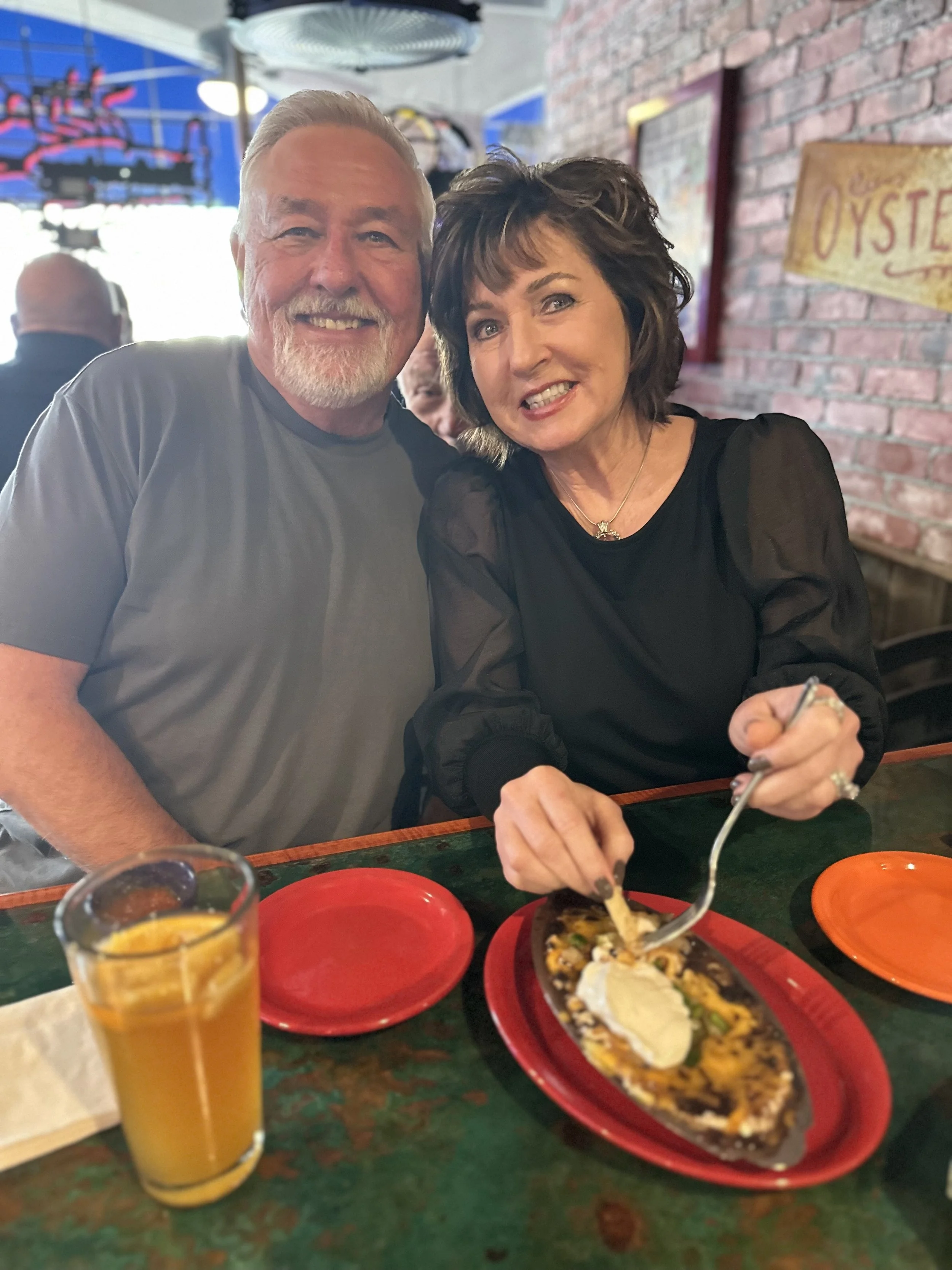 Two smiling people sitting at a restaurant table, eating black bean dip and a drink