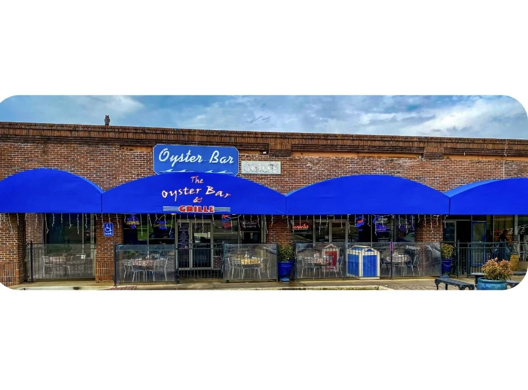 front entrance to the oyster bar & grille with blue awning, patio and coloful neon signage