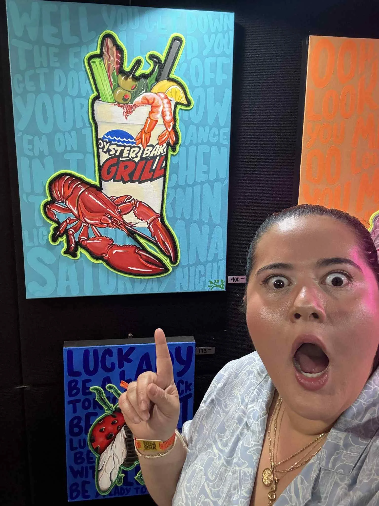 A woman with her mouth open and eyes wide pointing at a colorful poster of a seafood bucket with shrimp, lettuce, lemon, and a crawfish, with a large red crawfish illustration below.