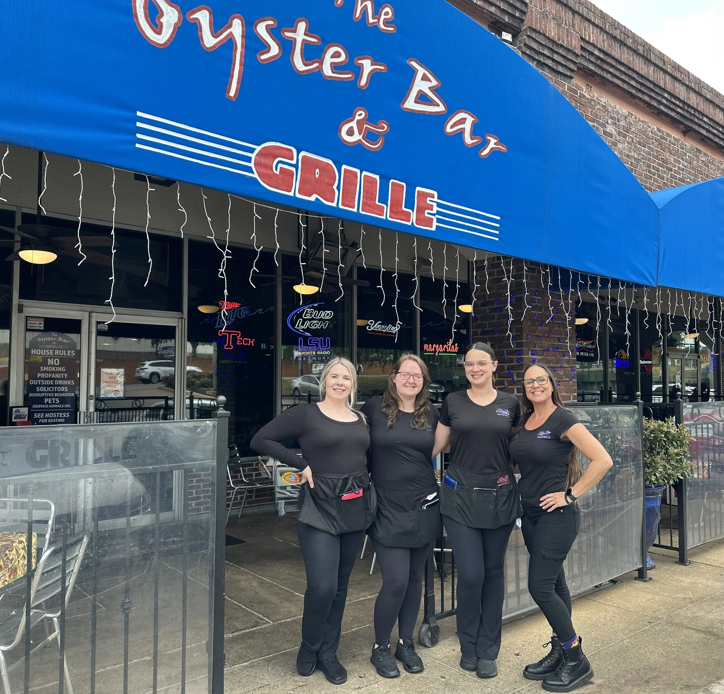Four women in black uniforms standing outside the Oyster Bar & Grill restaurant, smiling for the photo.