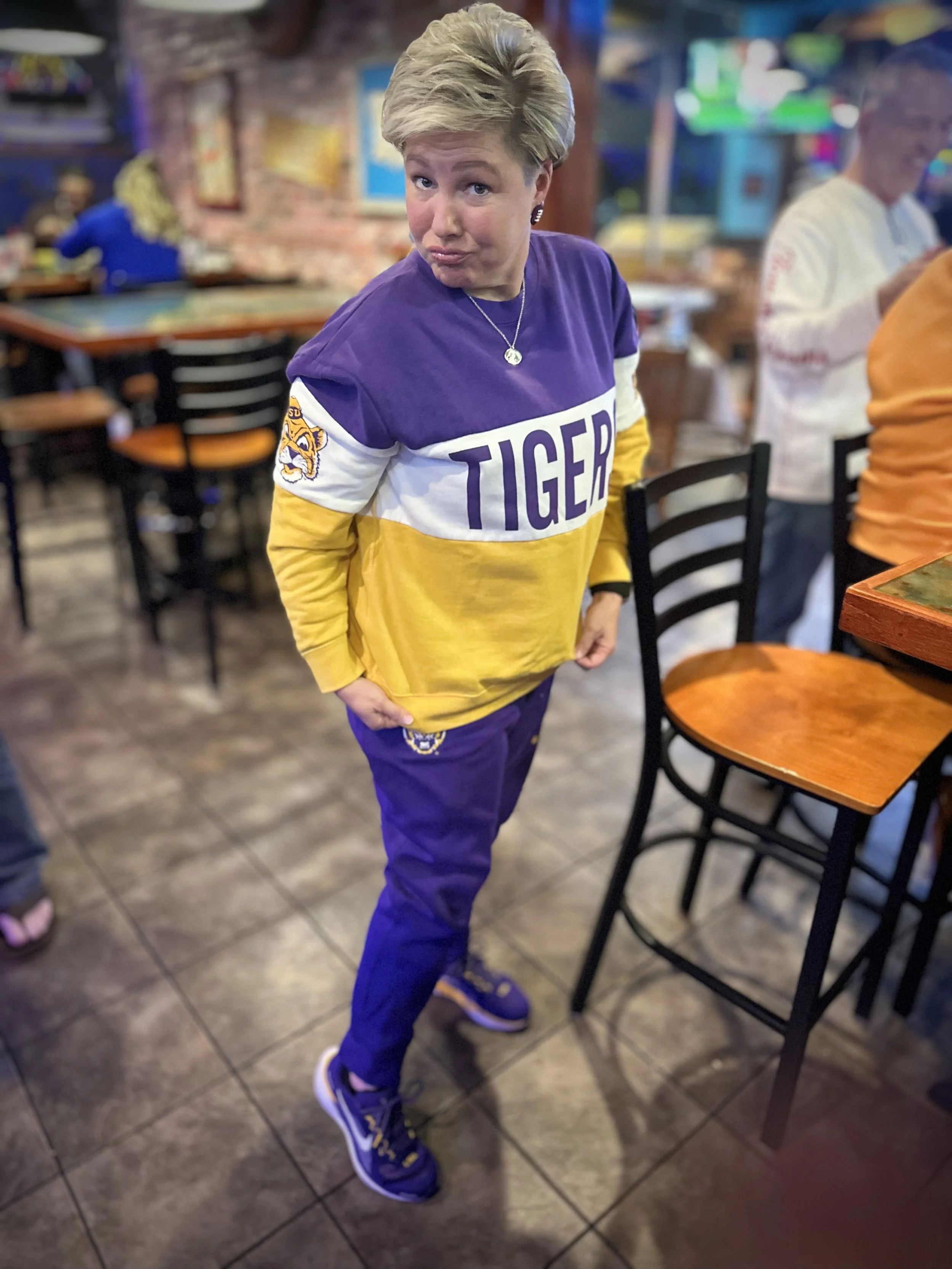 Person wearing LSU Tigers hoodie and athletic shoes standing inside a restaurant.