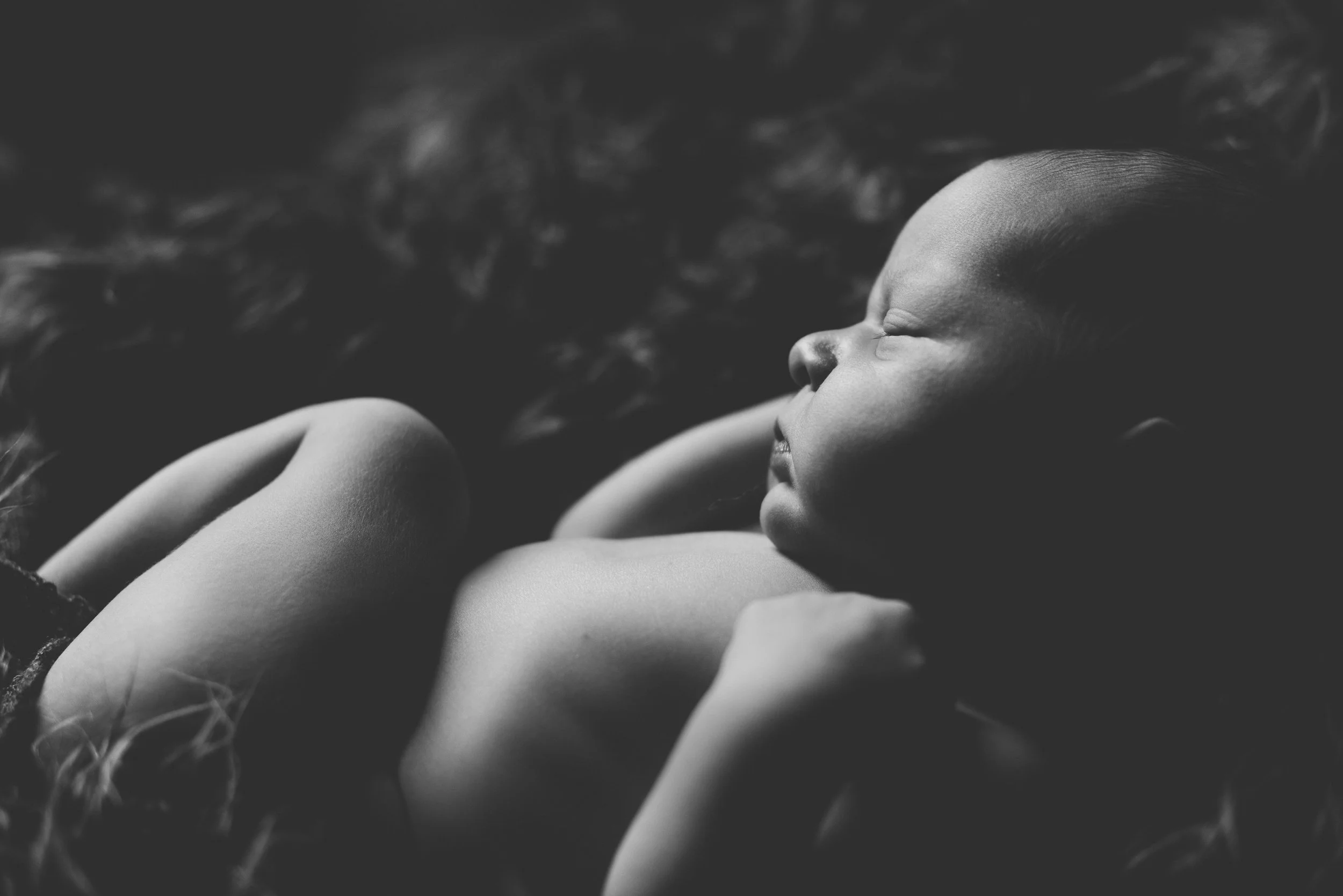 Close-up black and white photo of a woman's face in profile, lying down outdoors with her eyes closed and long hair spread out around her.