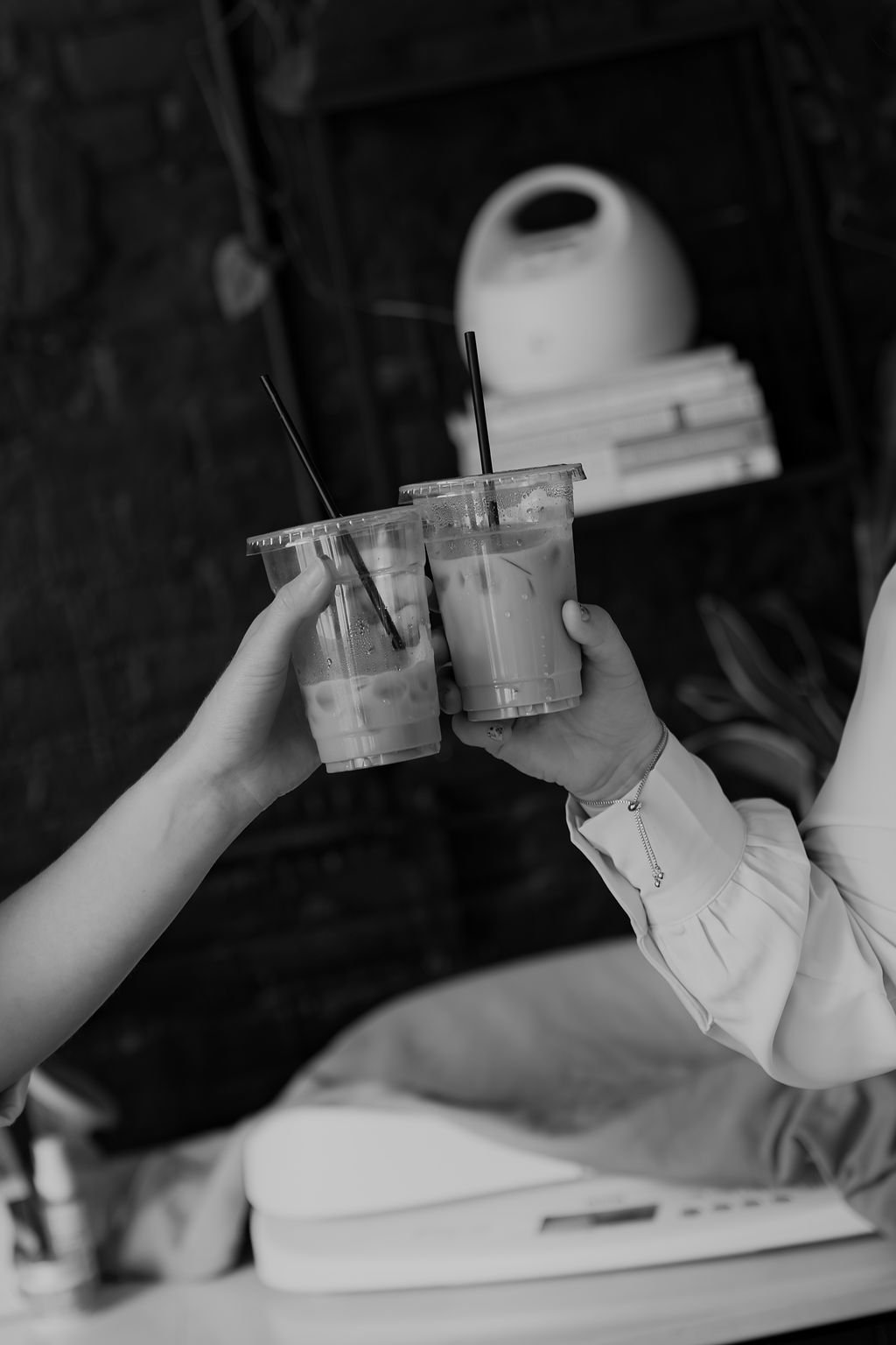 Two people clinking glasses filled with iced coffee or similar beverage, with straws, in an indoor setting.