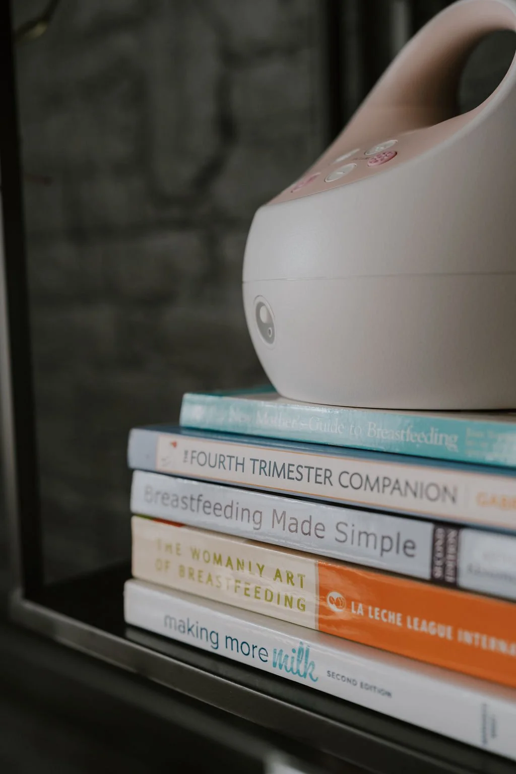 A stack of breastfeeding books with a breast pump on top.