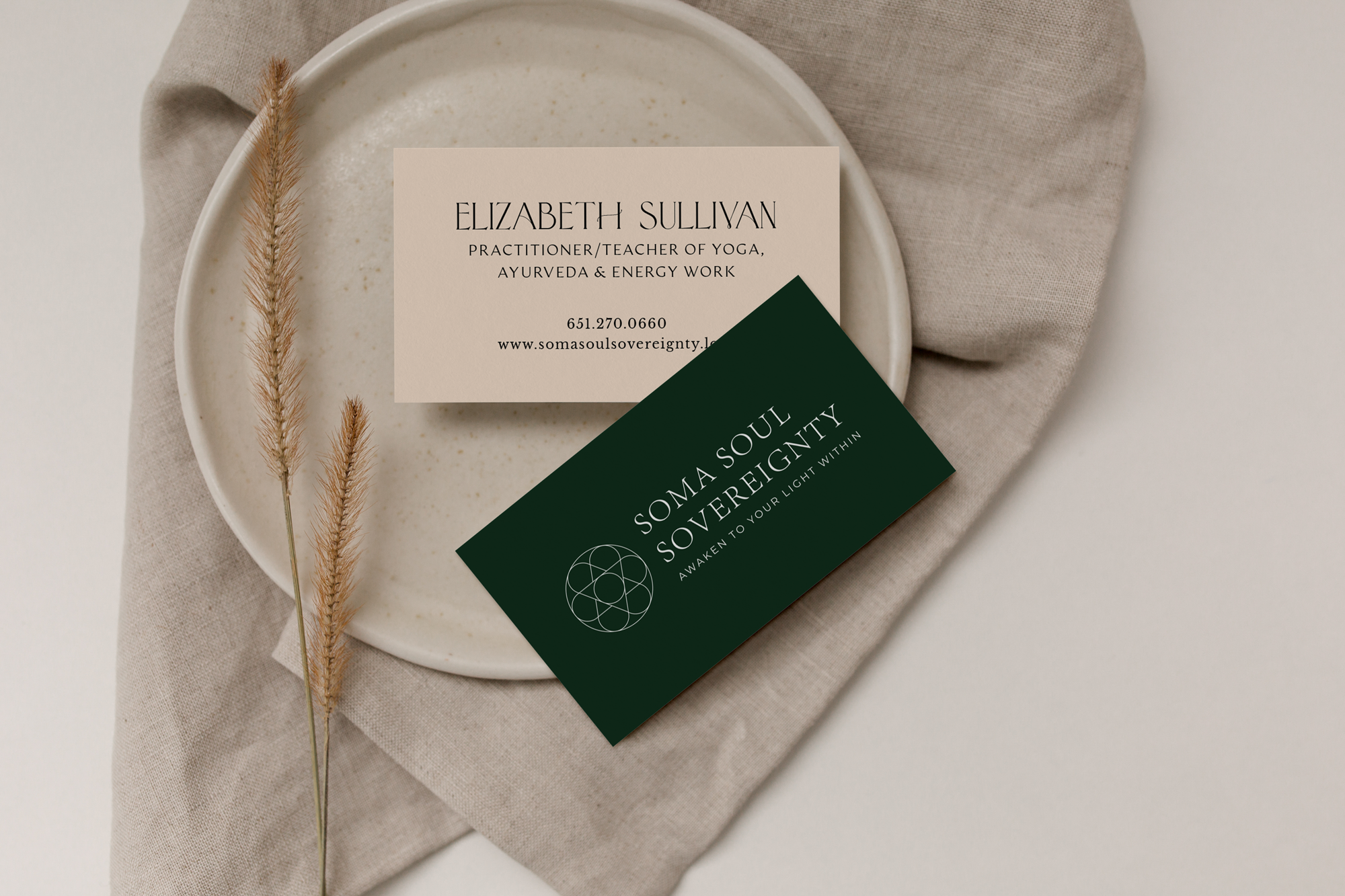 A sacred geometry designed logo on business card for Elizabeth Sullivan, a practitioner and teacher of yoga, Ayurveda, and energy work, placed on a beige cloth napkin with dried grass and a ceramic dish.